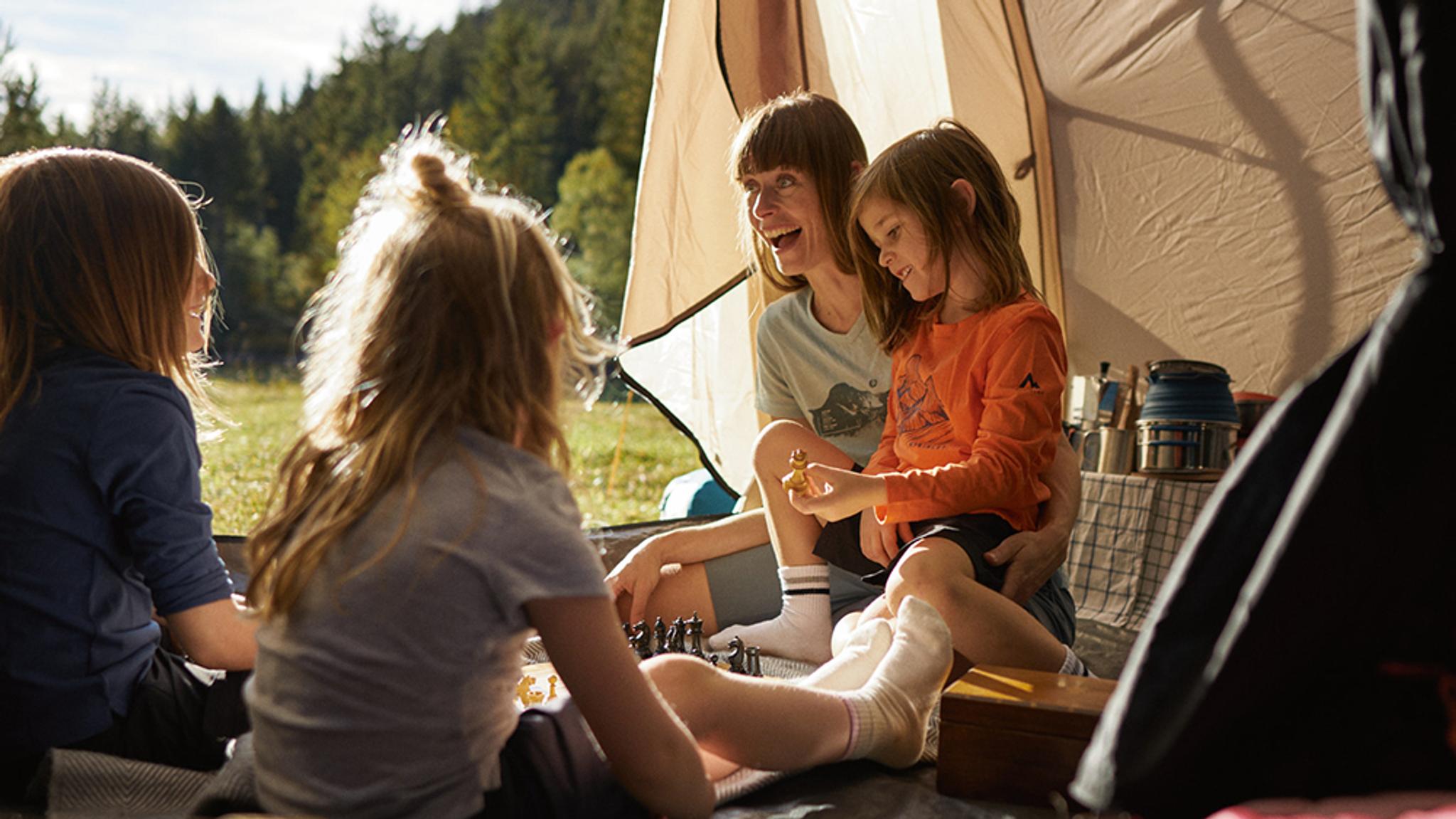 A mother and her three children happily playing chess inside a tent.