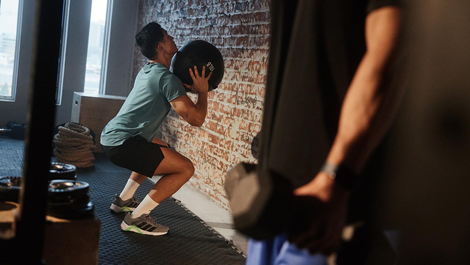 a man is squatting down while holding a medicine ball in a gym .