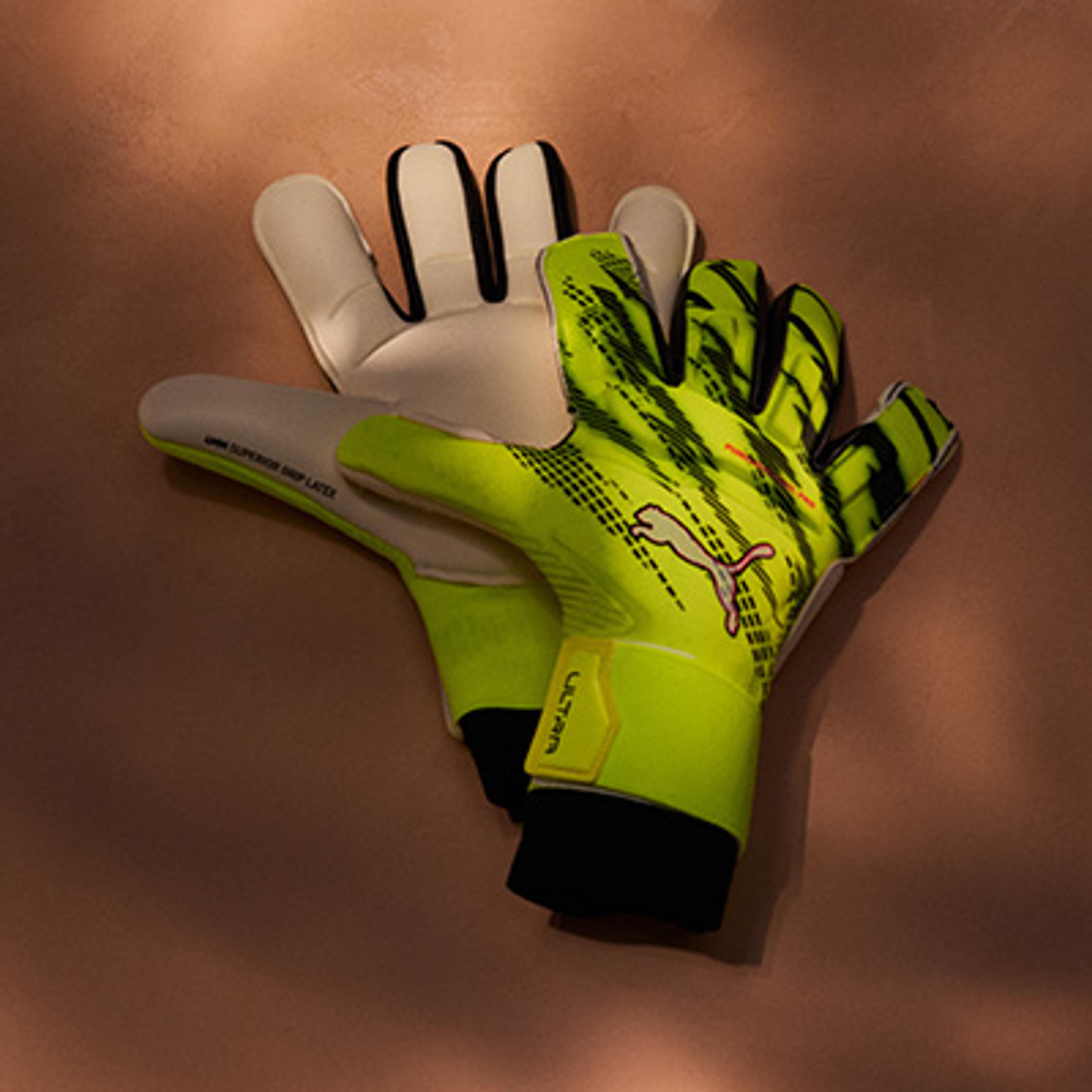 a man wearing a yellow and pink goalie glove is holding a soccer ball .