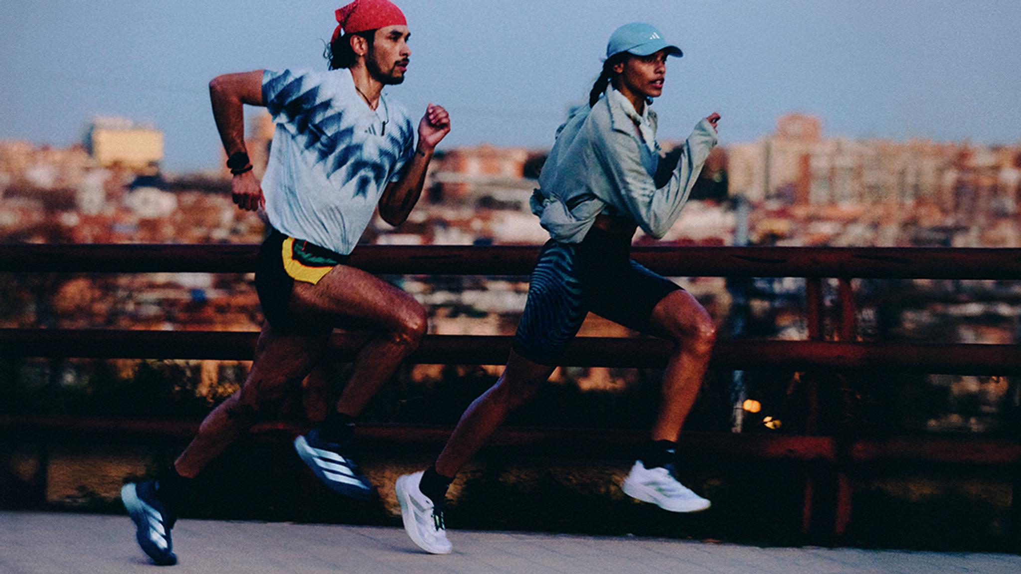 Two runners in Adidas athletic gear running outdoors with a city skyline in the background.