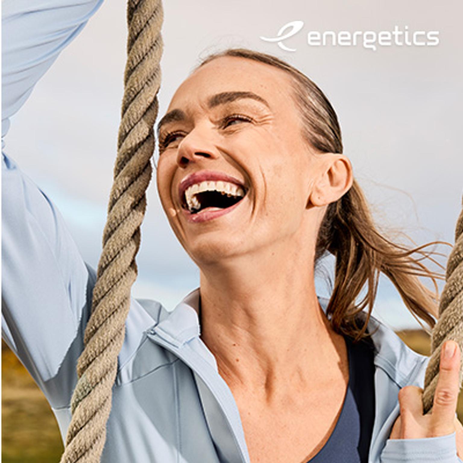 Woman in light blue athletic jacket laughing and holding a rope, with the Energetics logo.