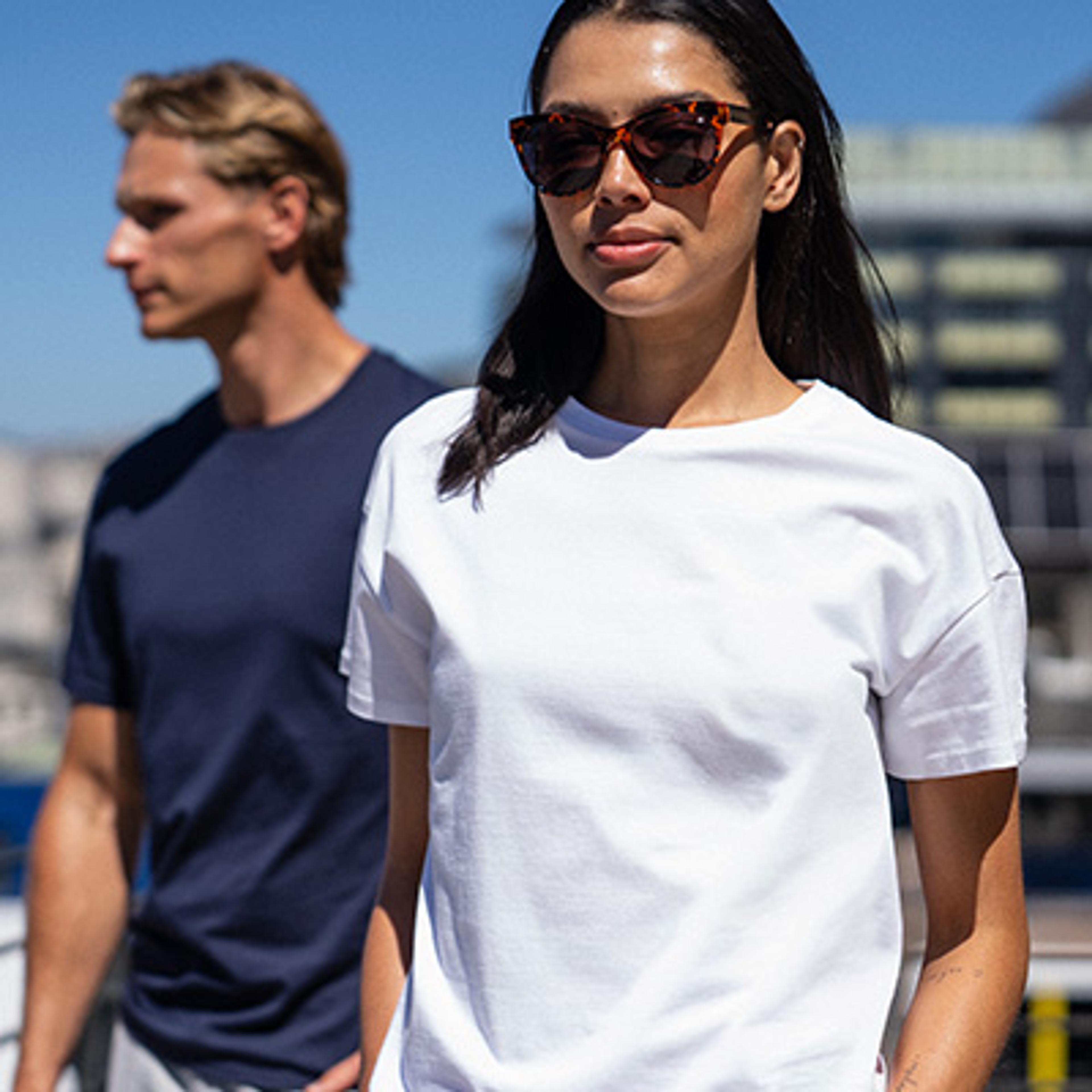 A woman in a white t-shirt and sunglasses stands in front of a man in a navy t-shirt.
