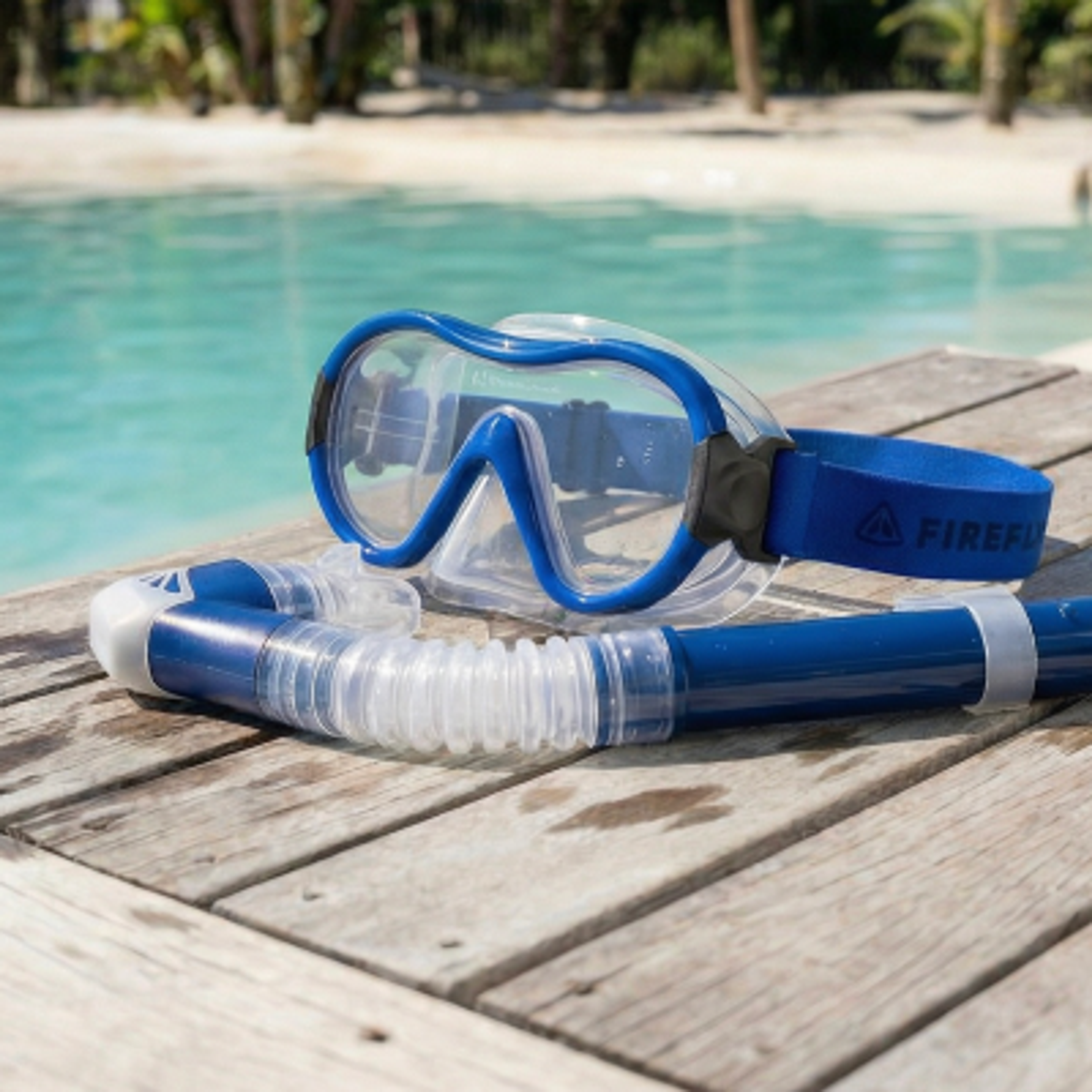 Blue snorkel mask and snorkel on a wooden deck by a pool.