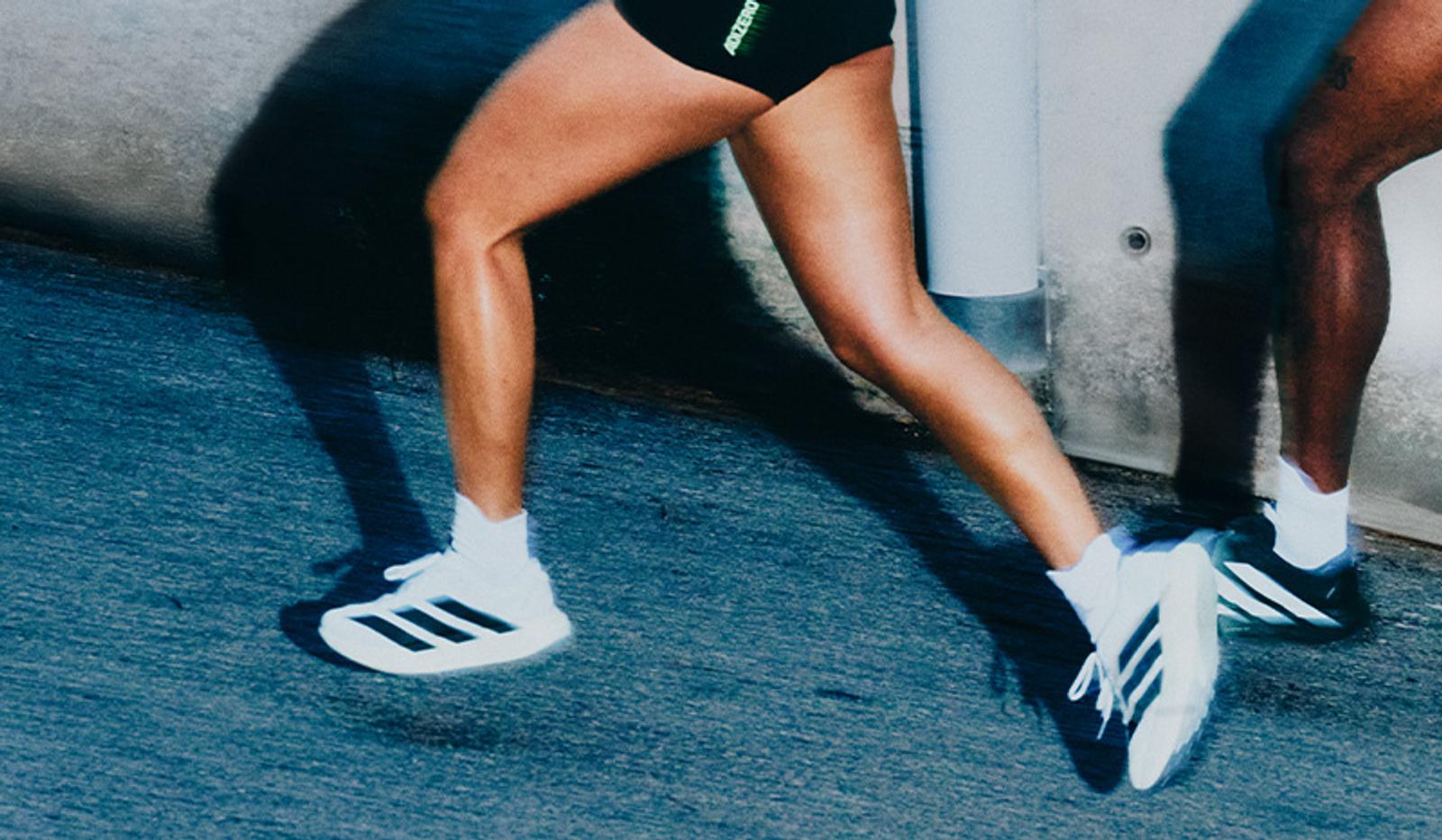 Two people running, showing their legs and Adidas sneakers in motion on a dark surface.
