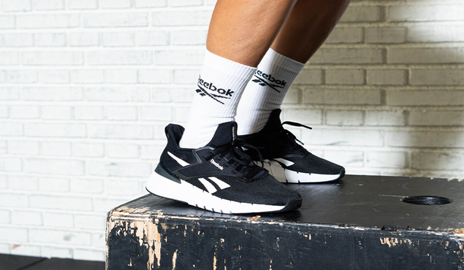 Black Reebok athletic shoes and white Reebok socks on a workout box.