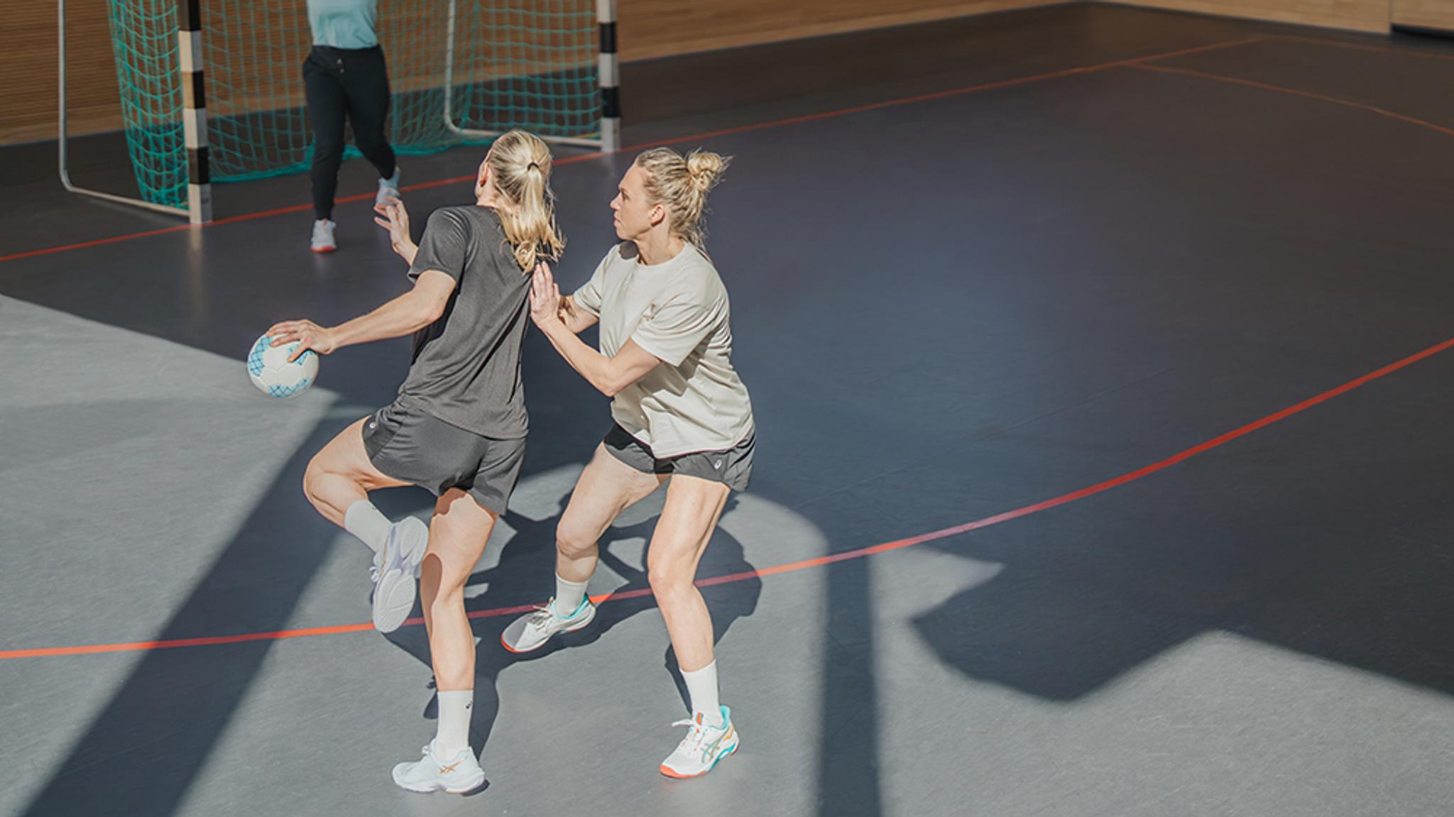 two women are playing handball on a court .