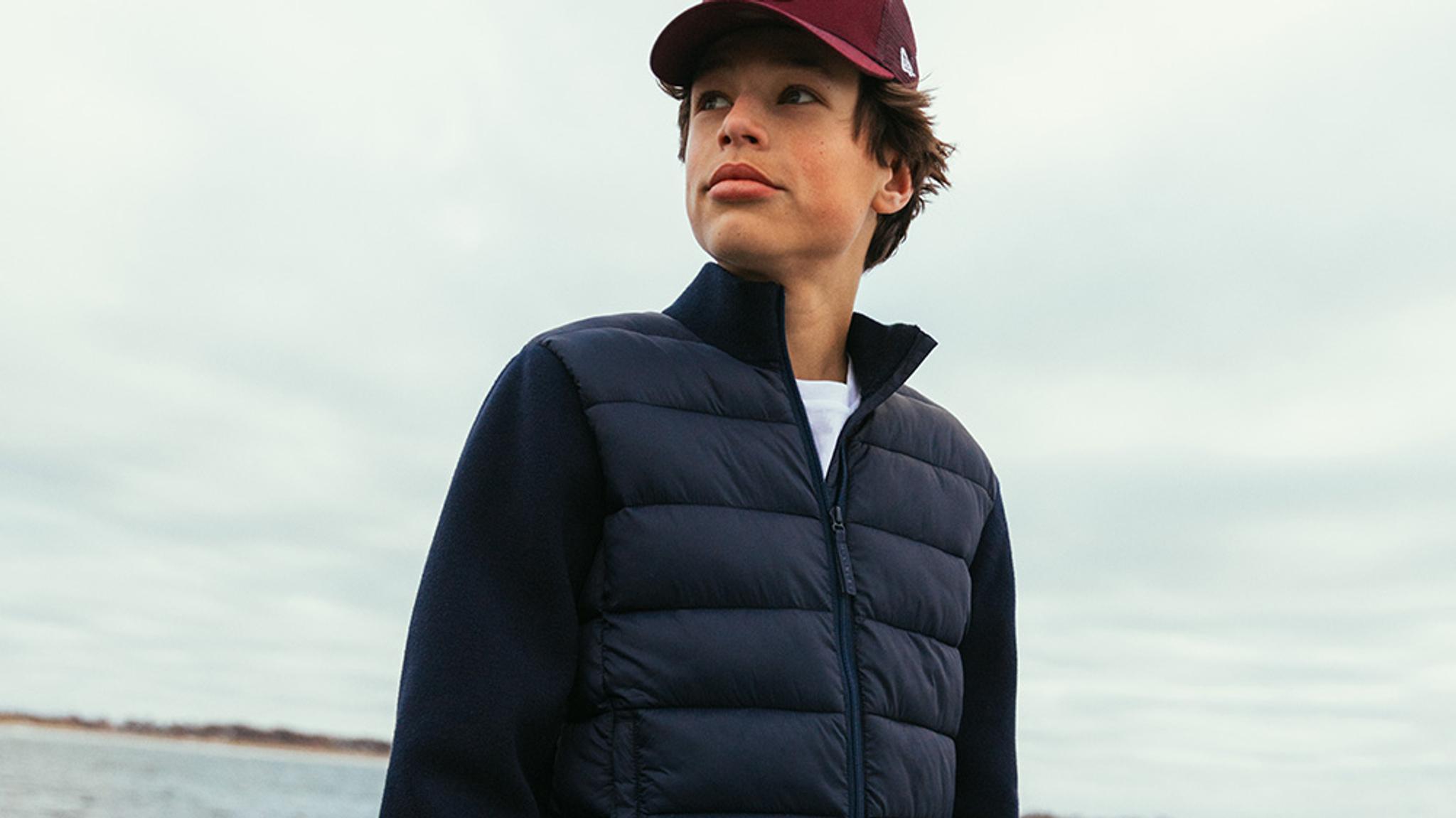 A young man wearing a red cap and a navy blue quilted jacket, outdoors.