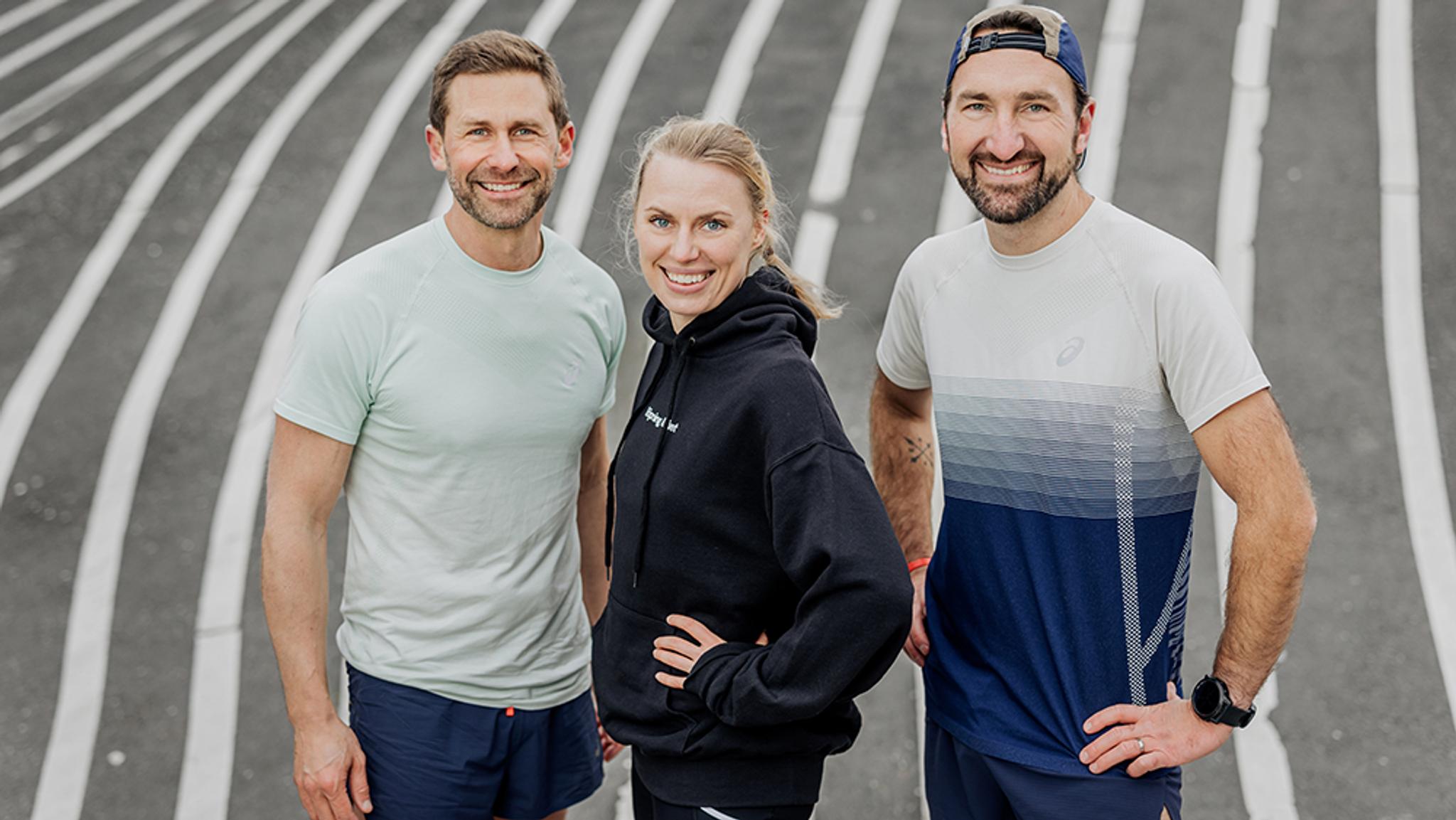 Three smiling runners, two men and one woman, standing on a track.