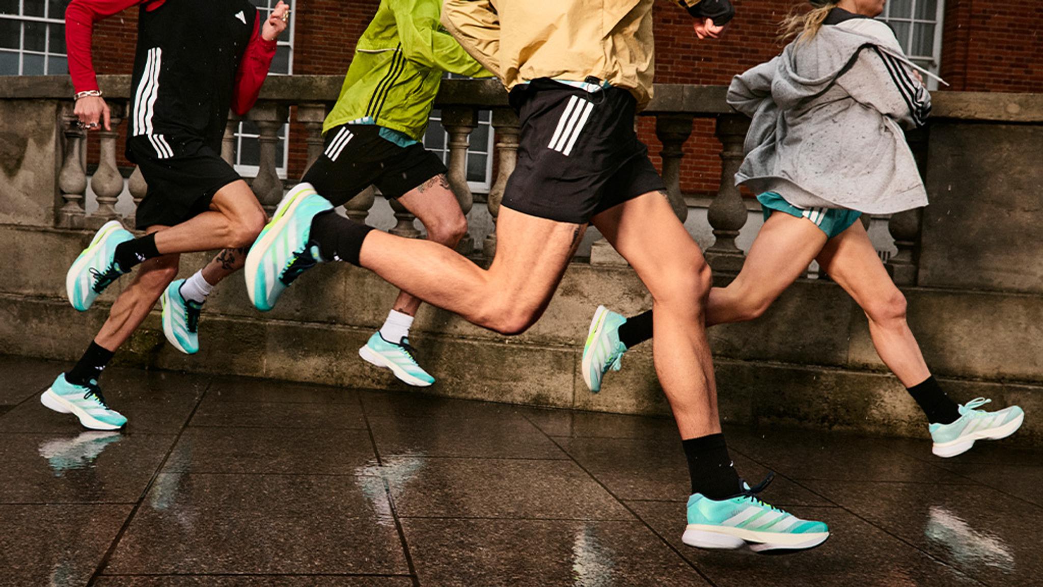 a group of people are running on a sidewalk wearing adidas shoes .