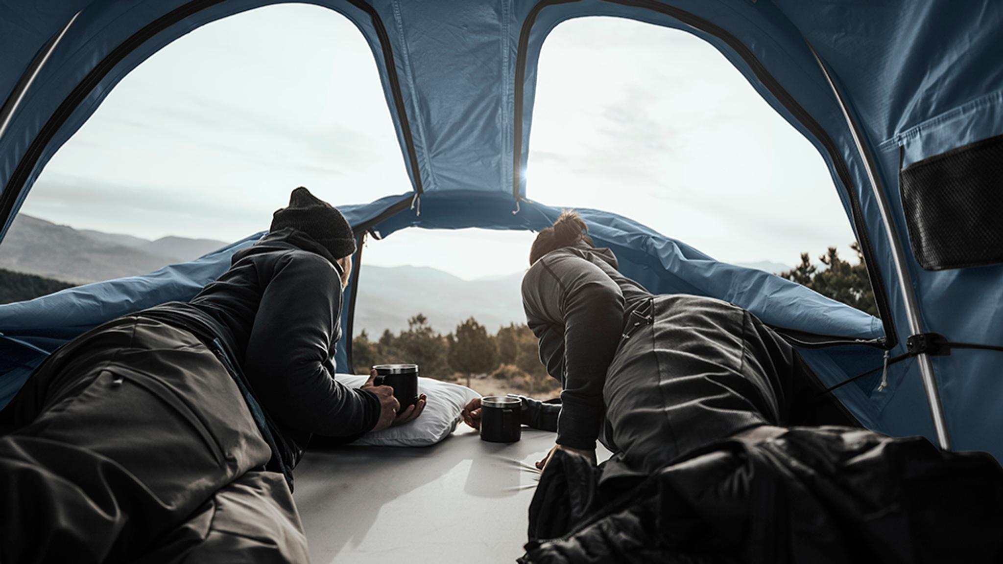 two people are laying in a tent with a view of the mountains .