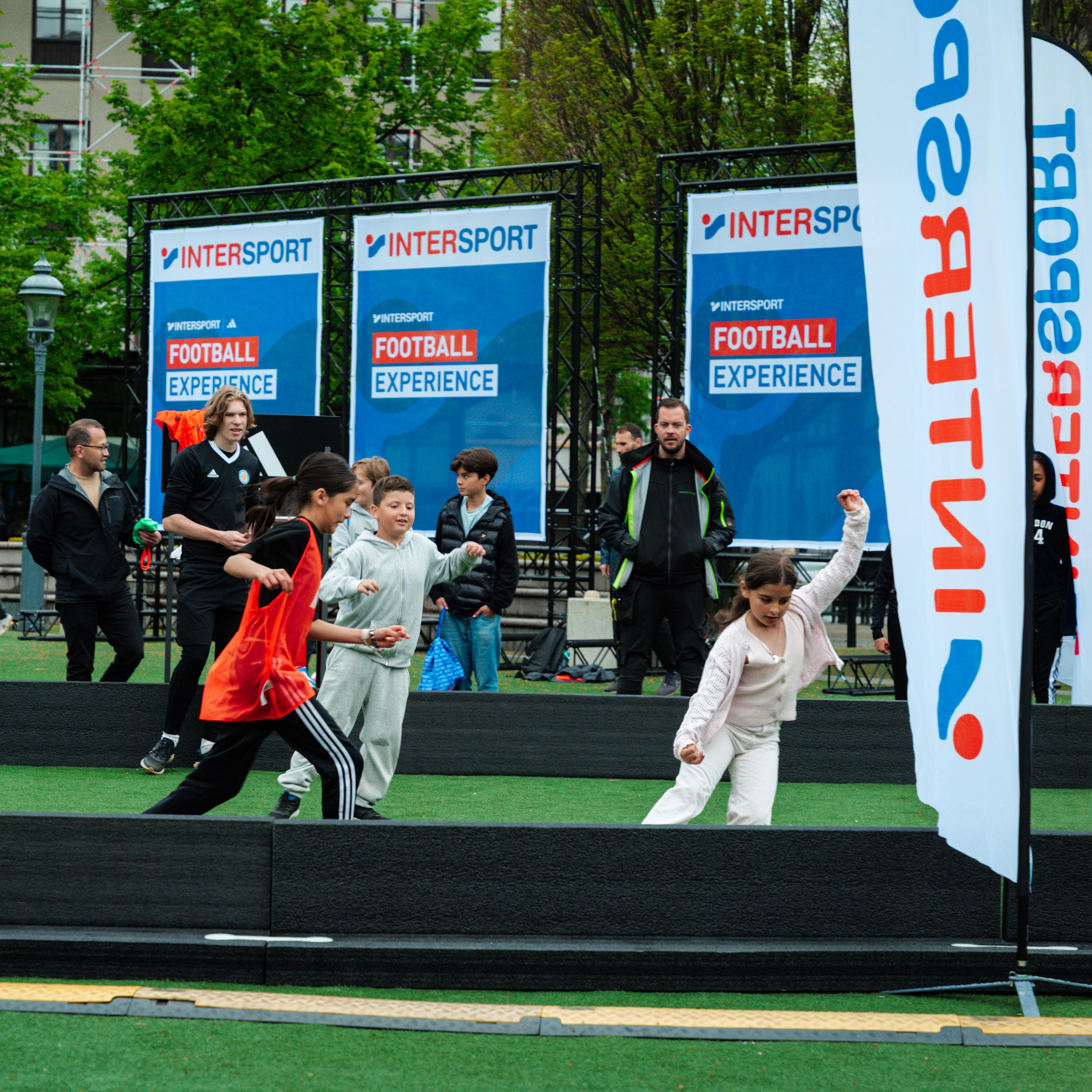 Children participate in an Intersport Football Experience event on an artificial turf field.