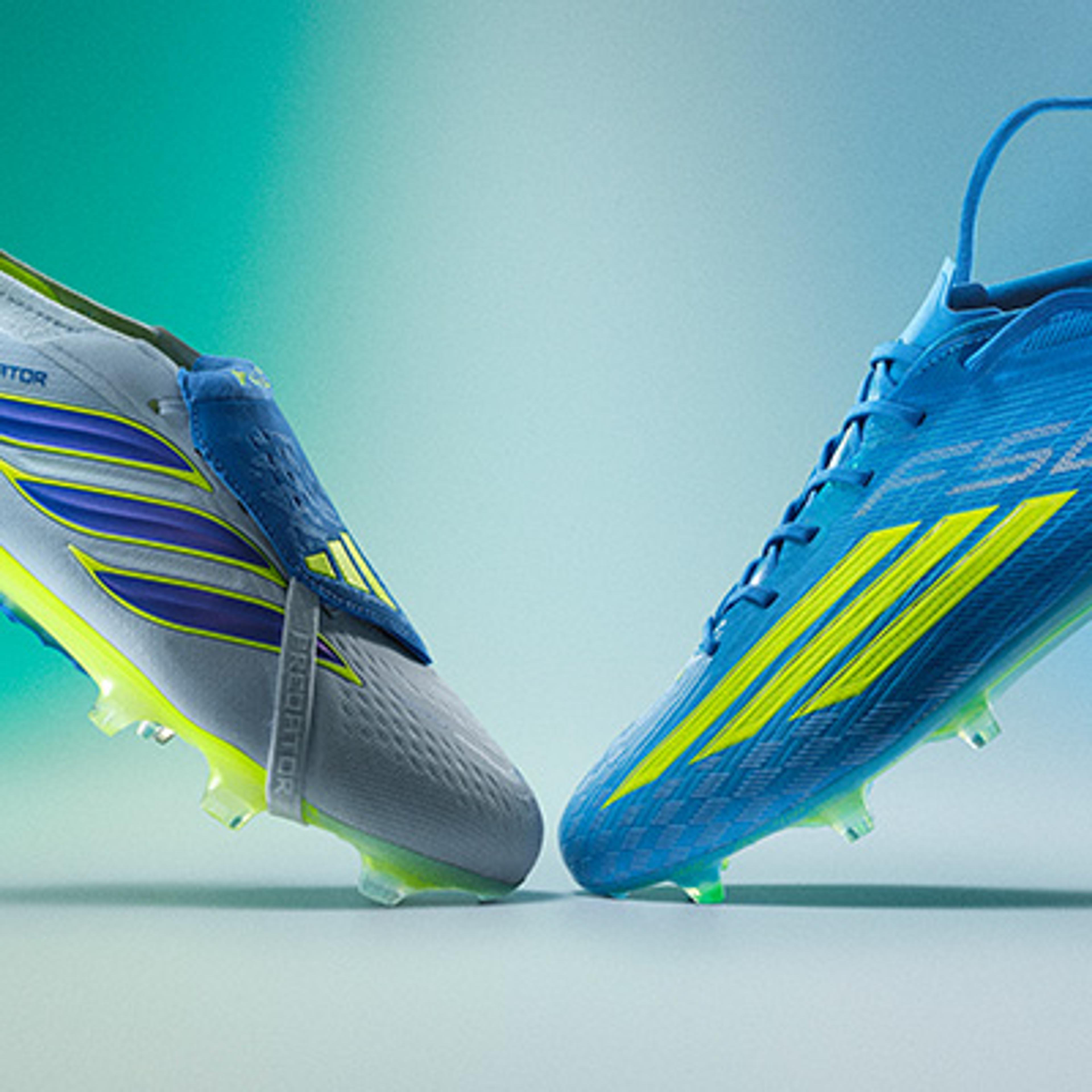 Two soccer cleats: a grey one with a blue flap and purple and yellow stripes, next to a blue one with yellow stripes. Both feature translucent green studs.