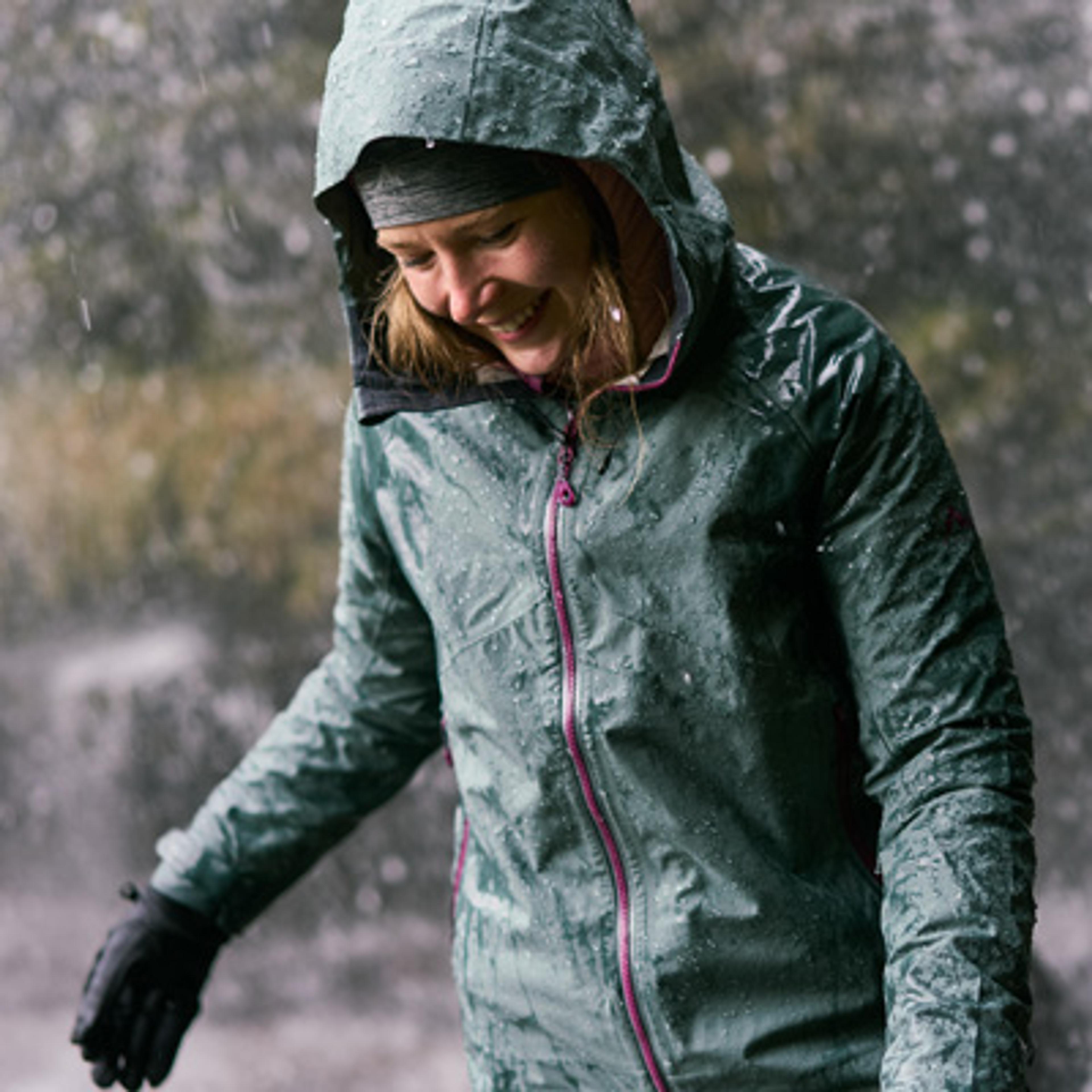 A smiling woman in a green rain jacket covered in raindrops.