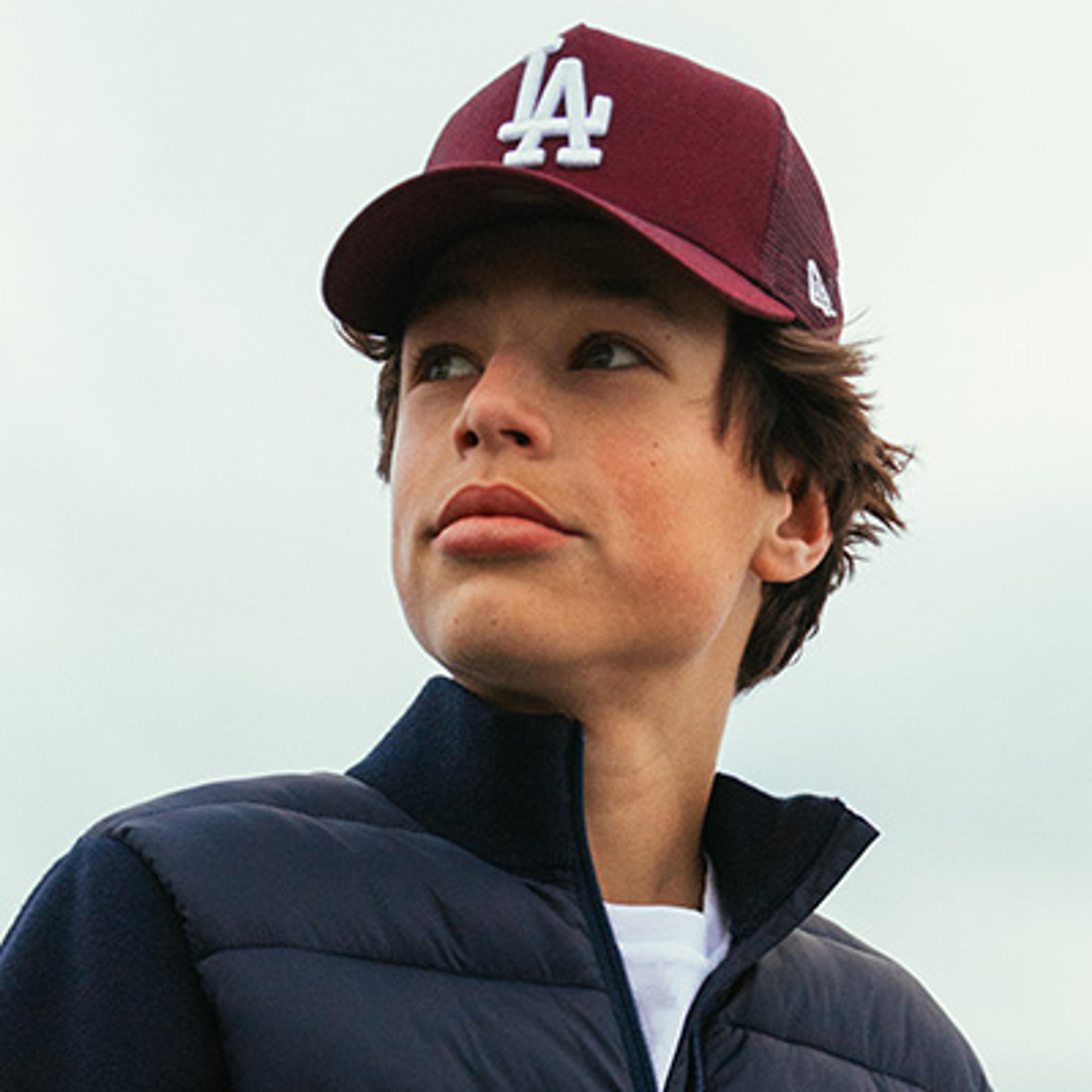 A boy wearing a maroon 'LA' baseball cap and a navy puffer jacket looks up and to the left.