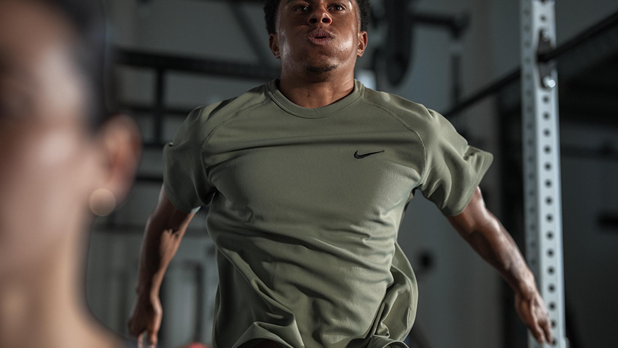 A man in a green Nike shirt jumps during a gym workout.