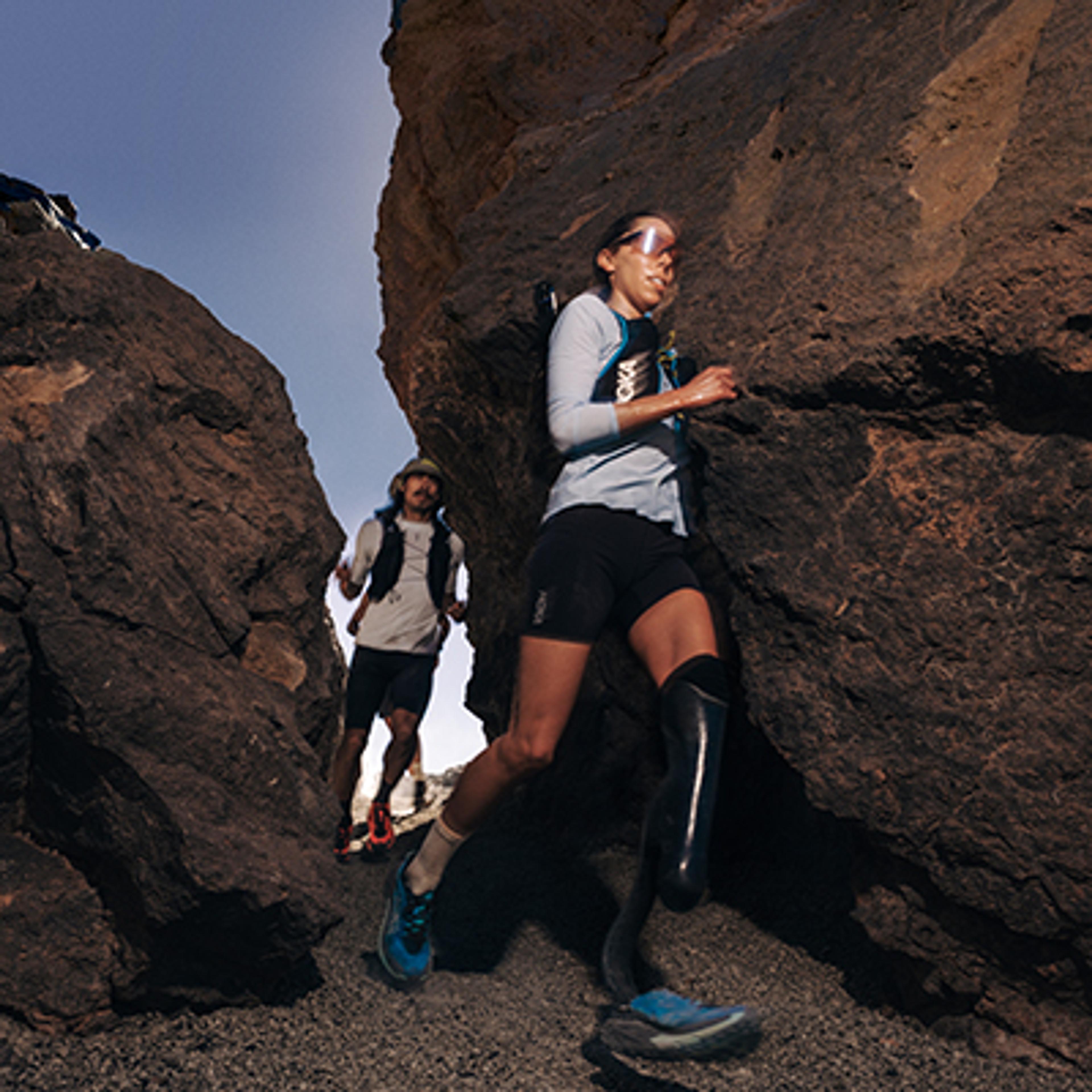 a man and a woman are running through a rocky canyon .