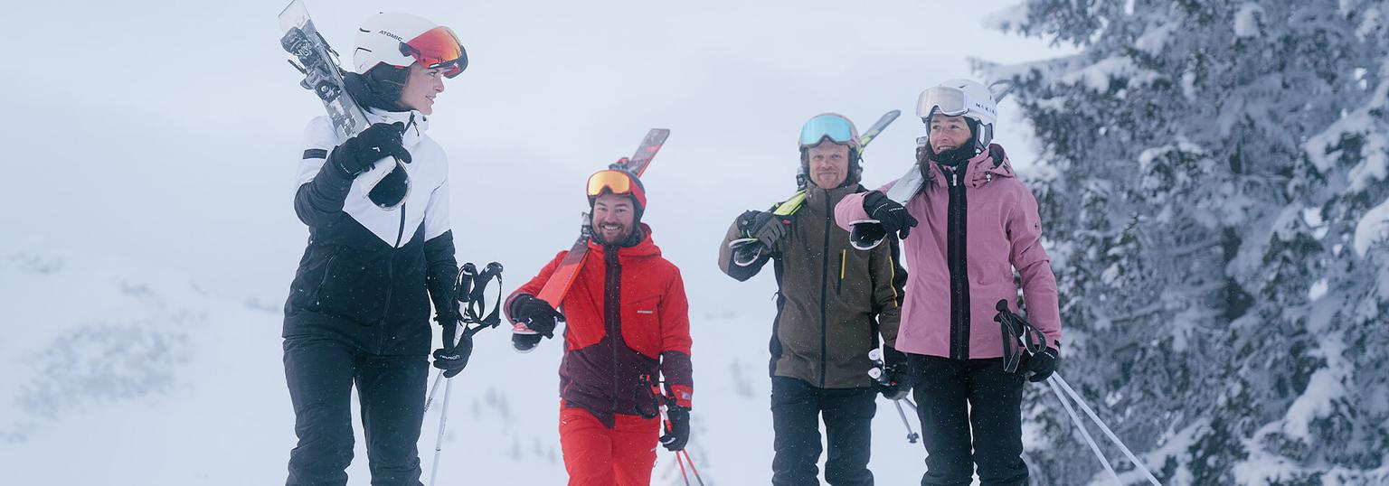 Fyra personer går i snön med skidutrustning på sig