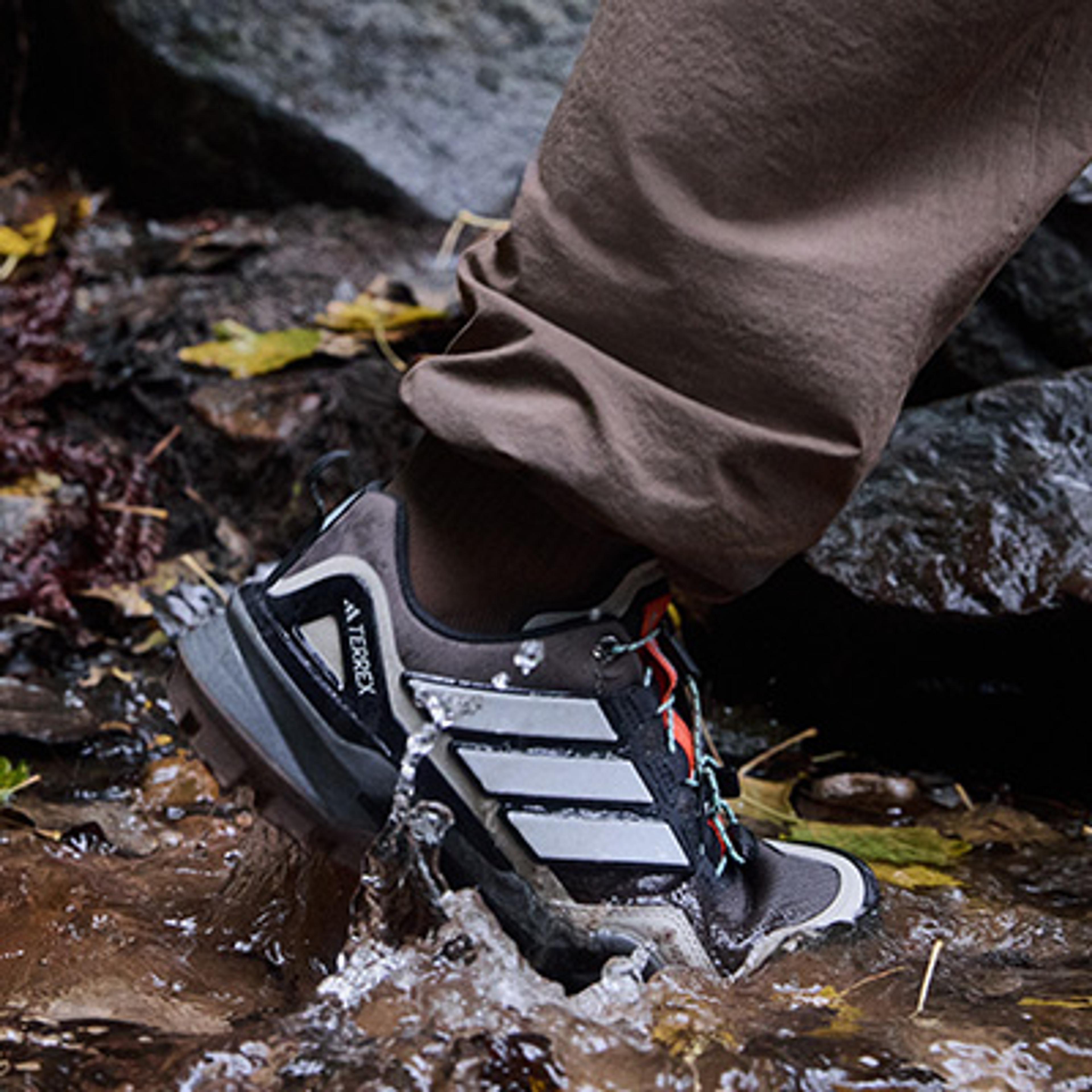 a person wearing a pair of adidas terrex shoes is walking through a puddle of water .
