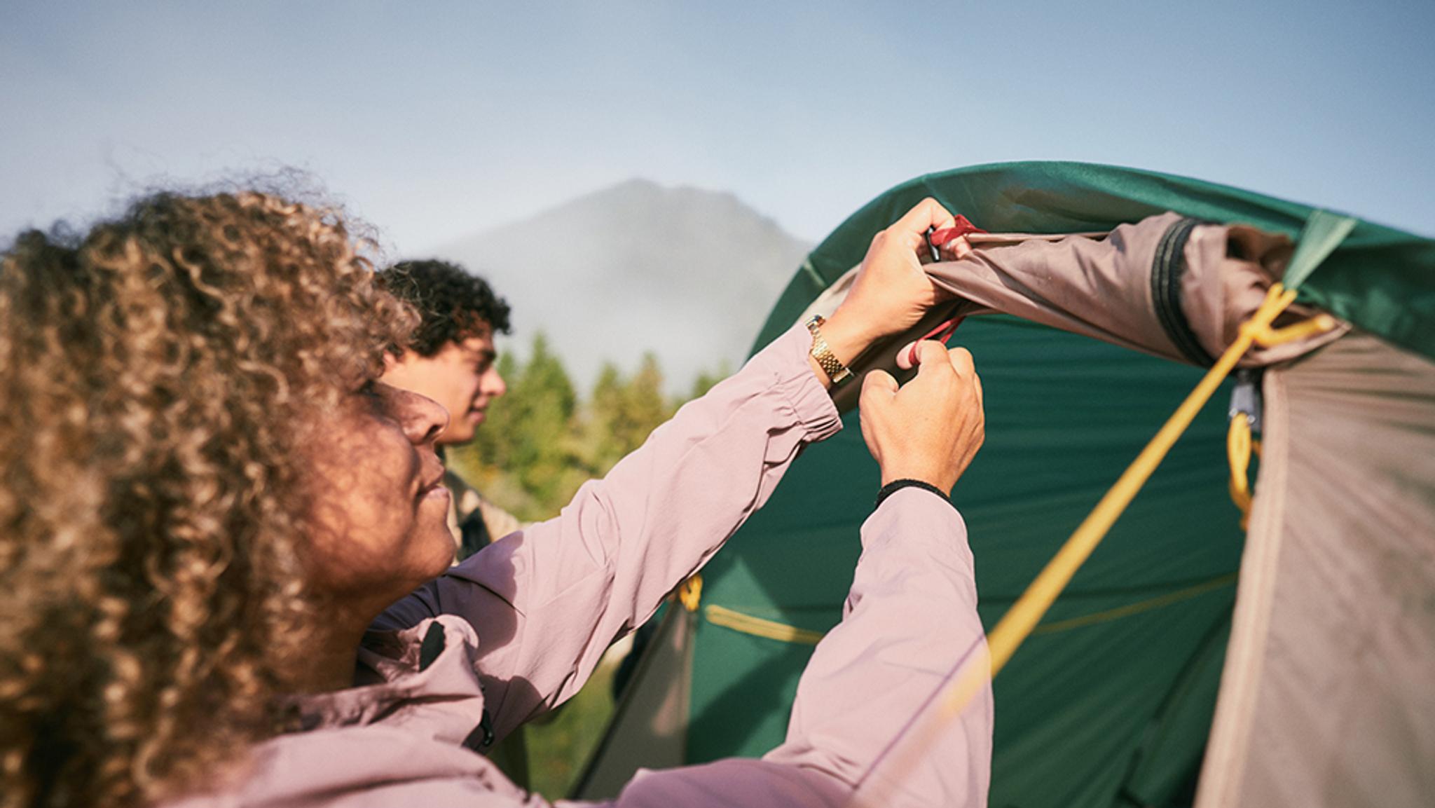 Two people setting up a camping tent outdoors.