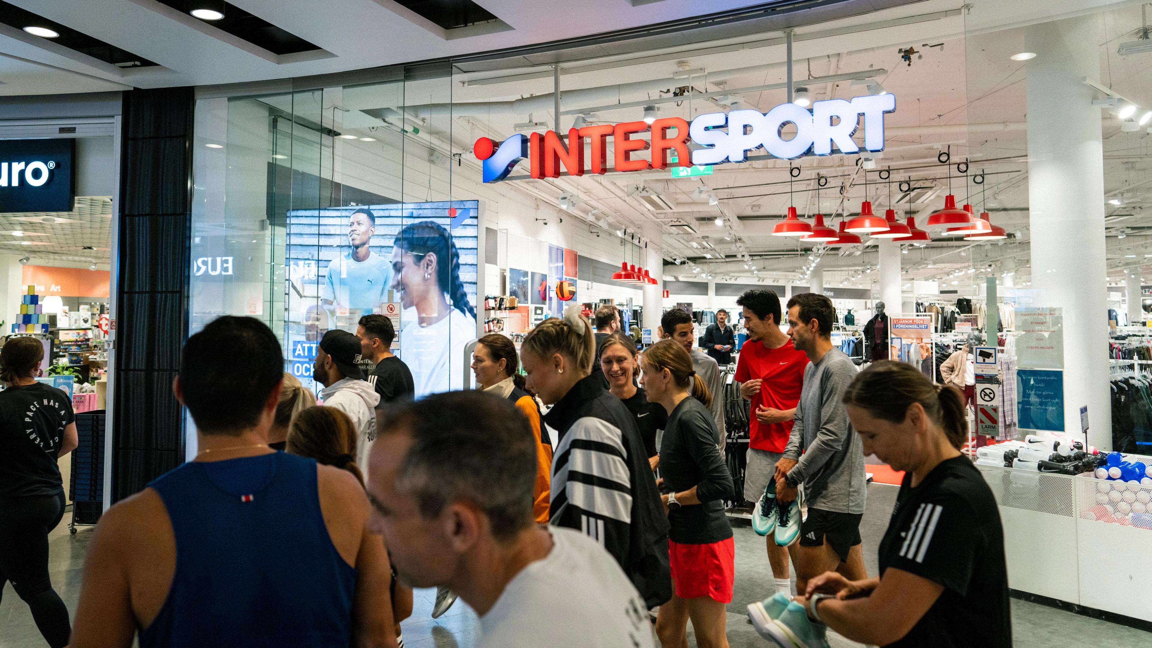 a group of people are standing outside of an intersport store .