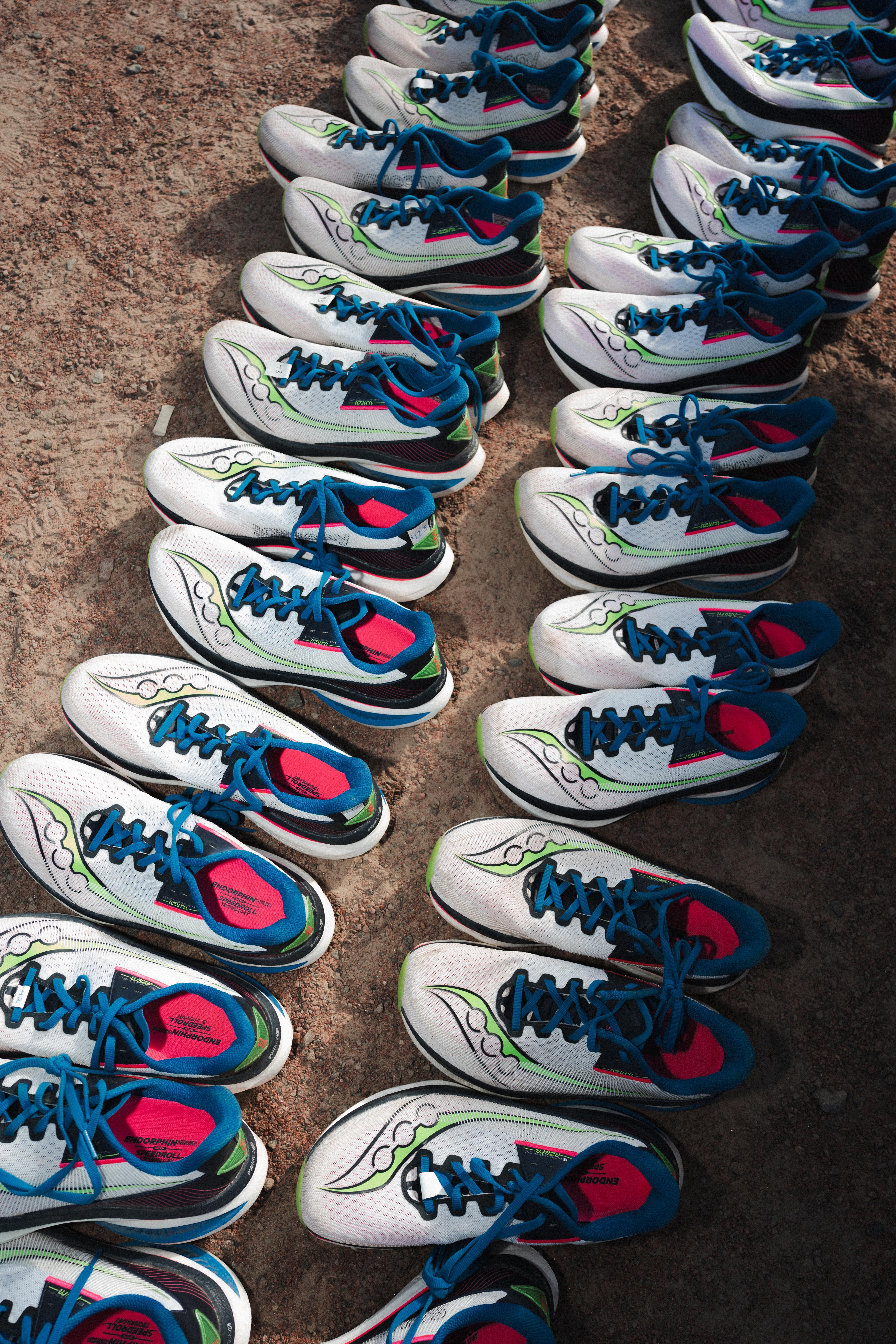 Rows of white, blue, and green running shoes on a dirt path.
