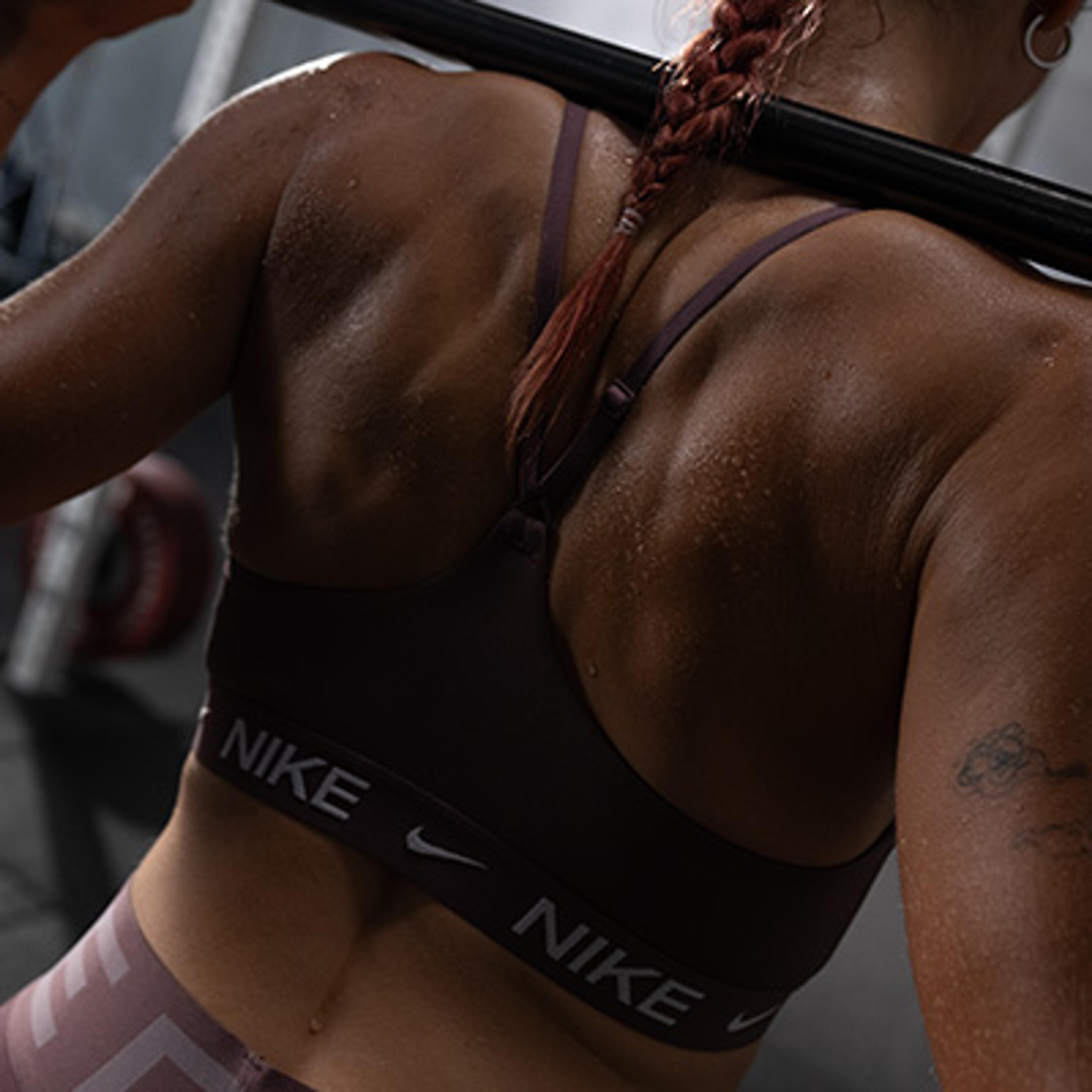 Close-up of a person's sweaty back and shoulders in a Nike sports bra, holding a barbell.