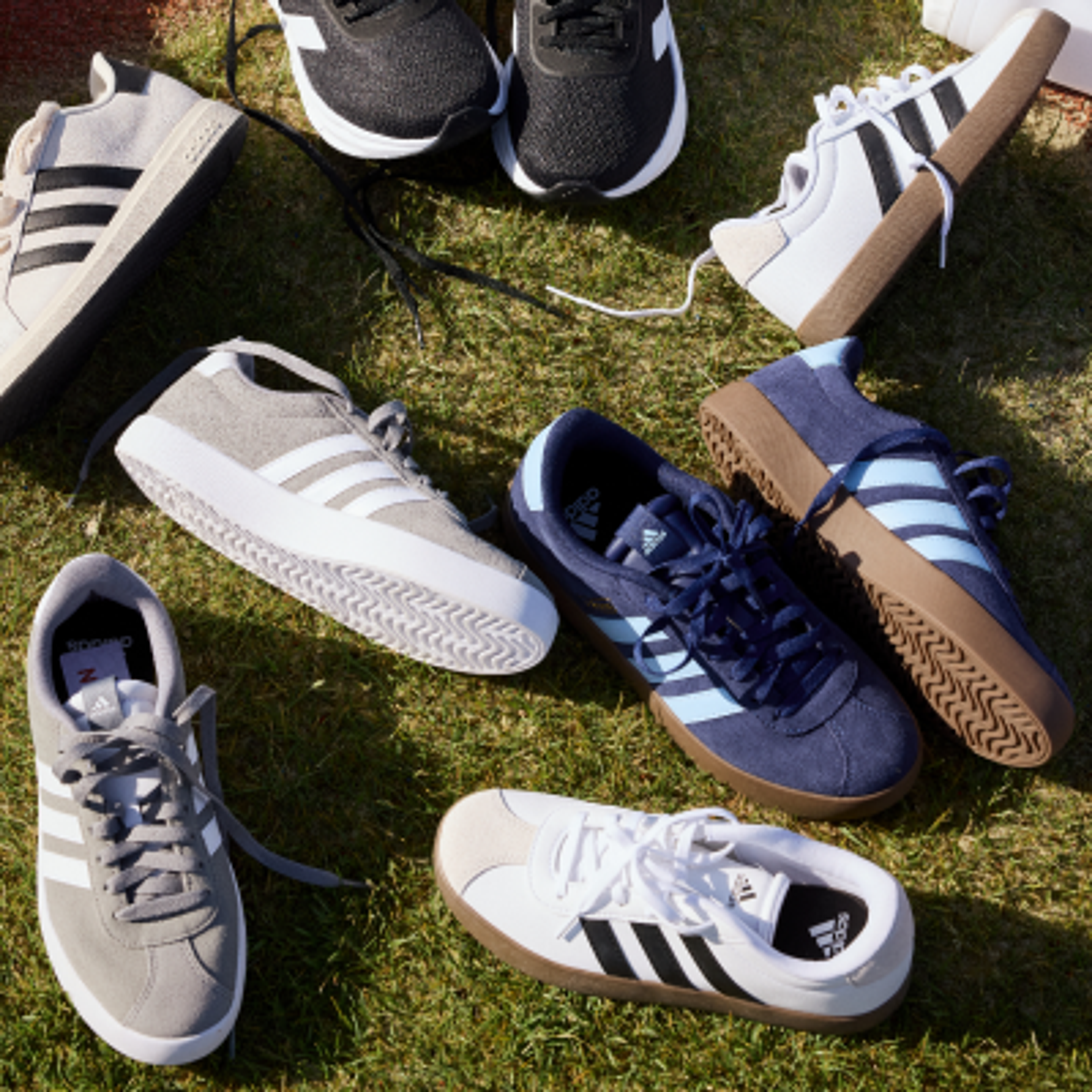 Multiple pairs of Adidas sneakers in various styles and colors scattered on green grass.