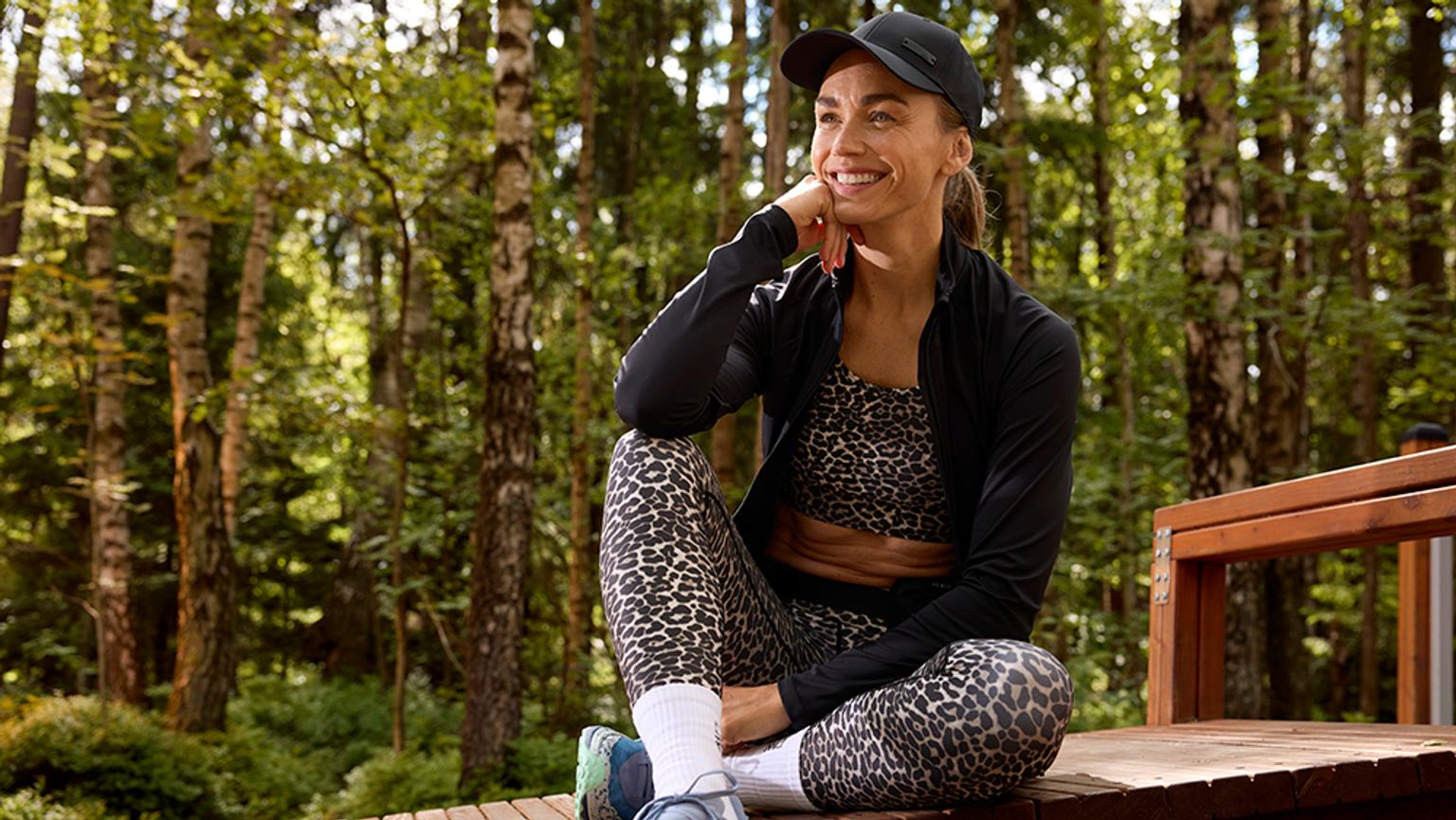 a woman is sitting on a wooden bench in the woods .