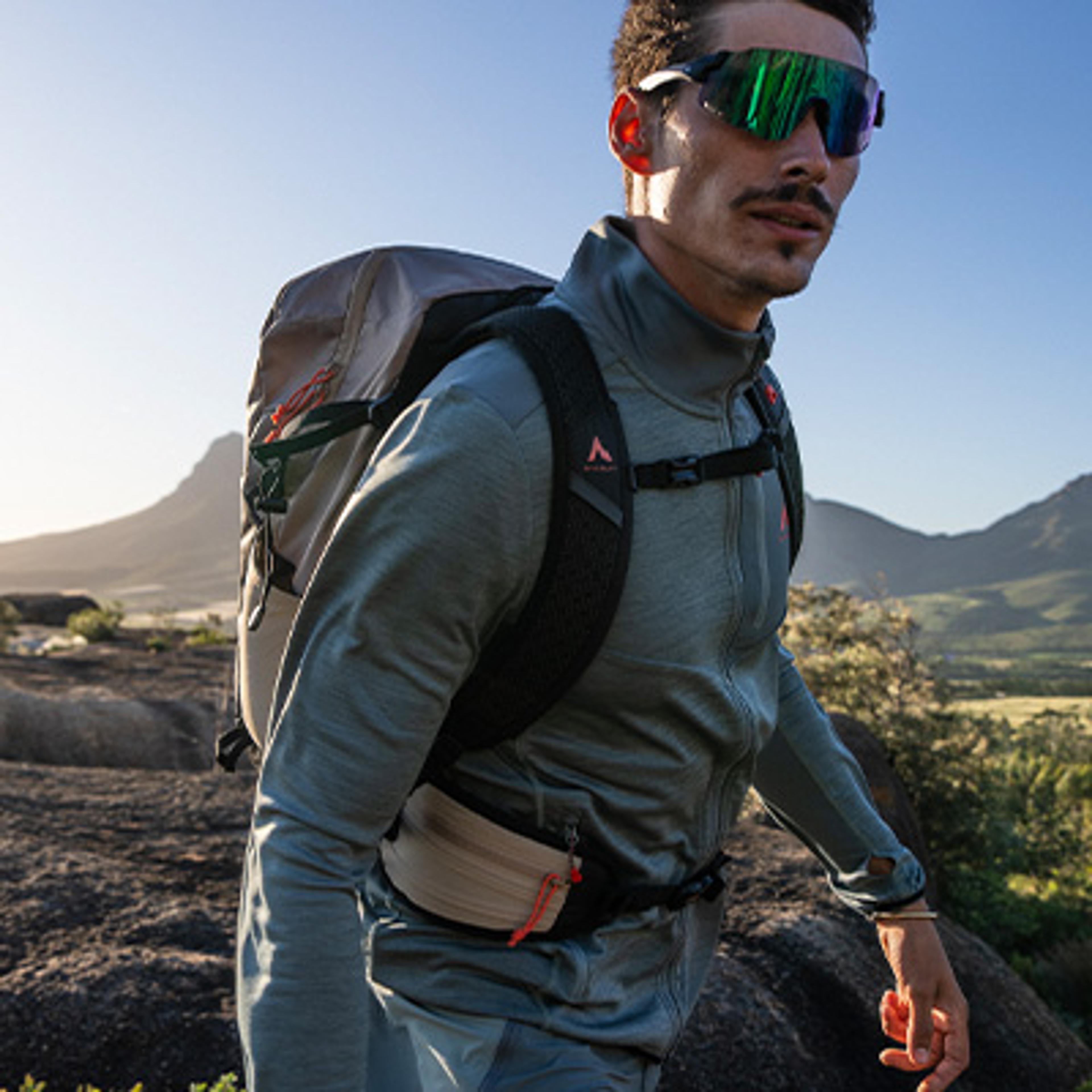 Man hiking with a backpack and mirrored sunglasses on a rocky trail.