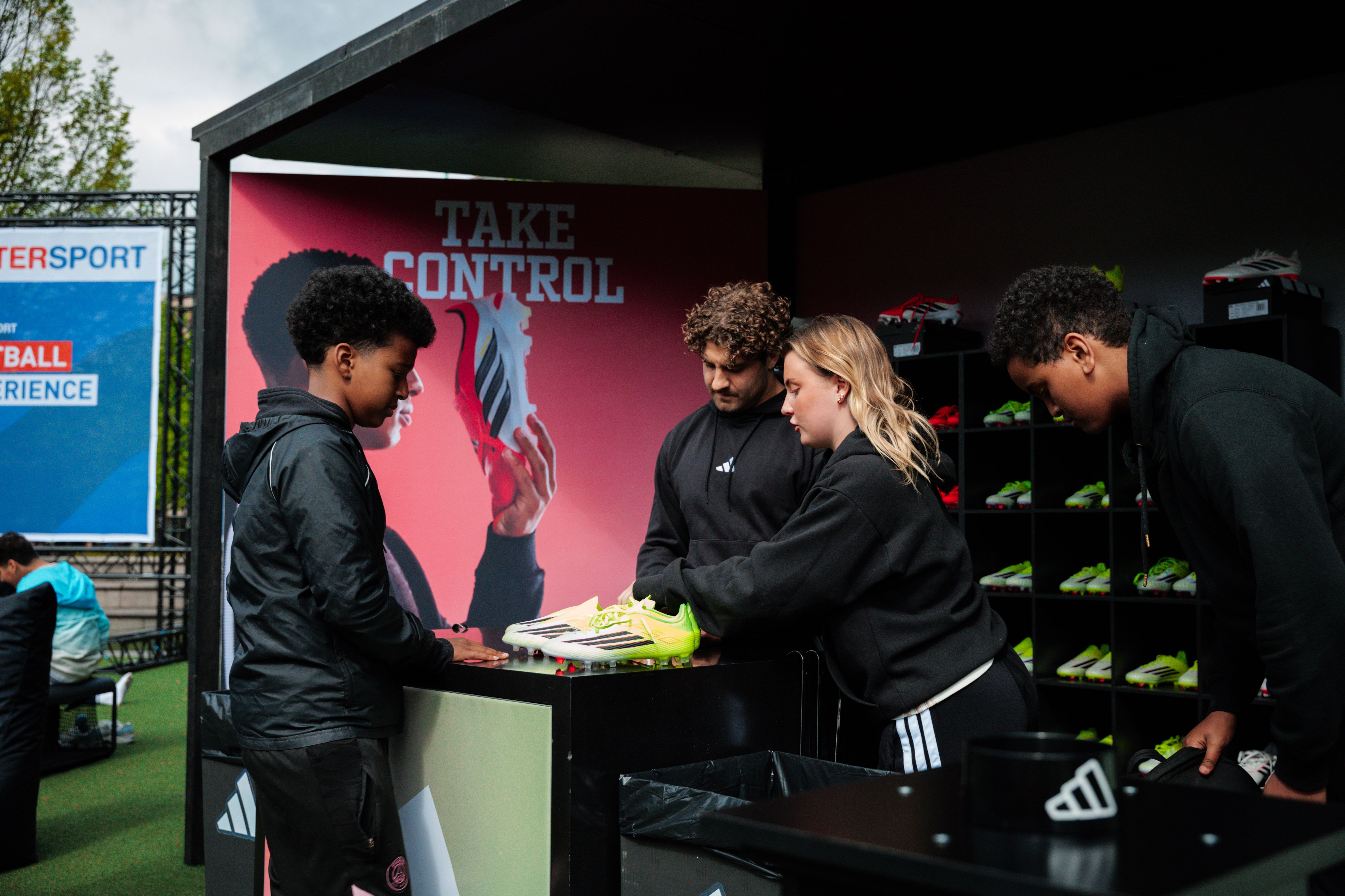 A boy and three adults examine bright green Adidas soccer cleats at an outdoor event booth.