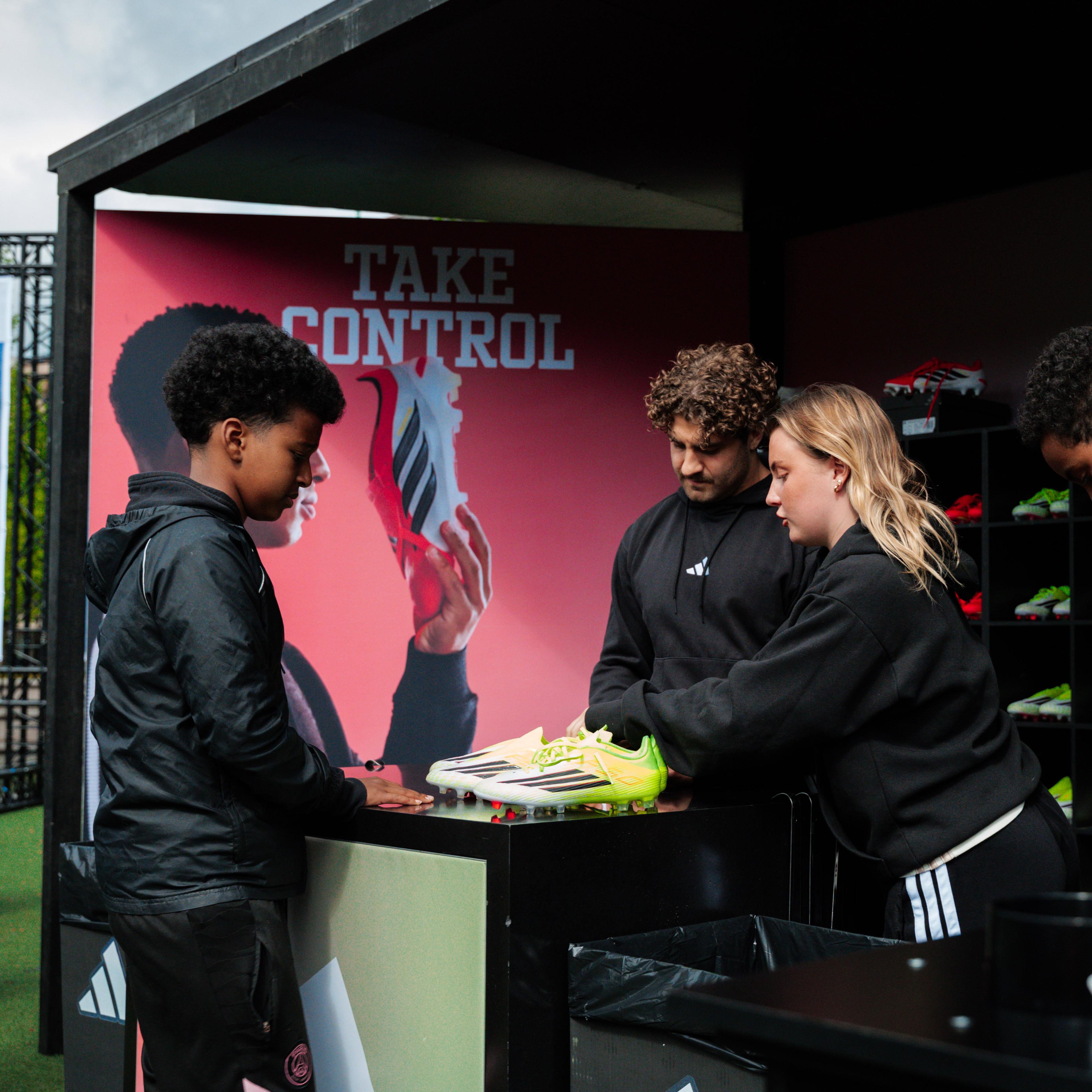 A boy and three adults examine bright green Adidas soccer cleats at an outdoor event booth.