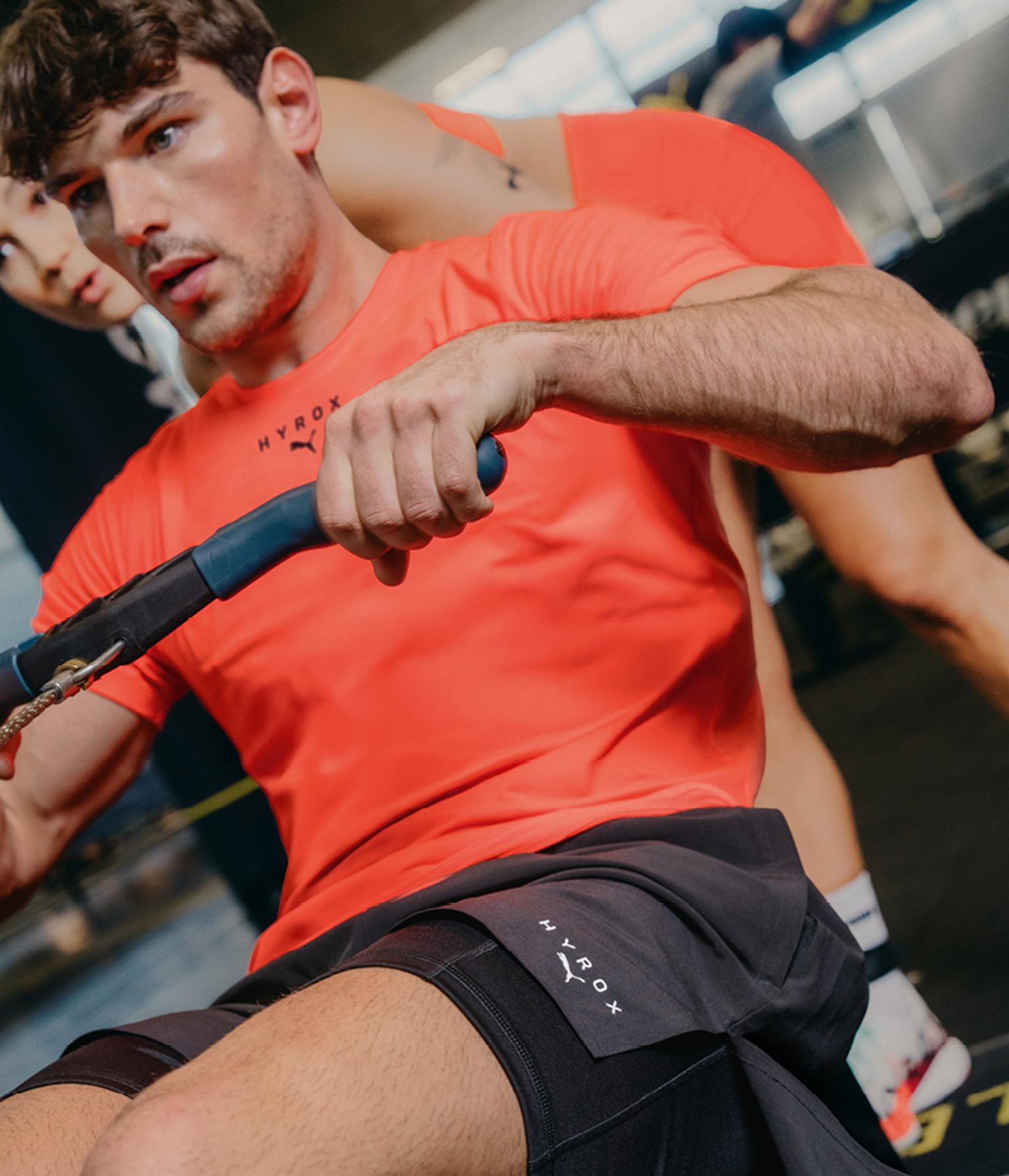 a man in a red shirt and black shorts is rowing a boat in a gym .