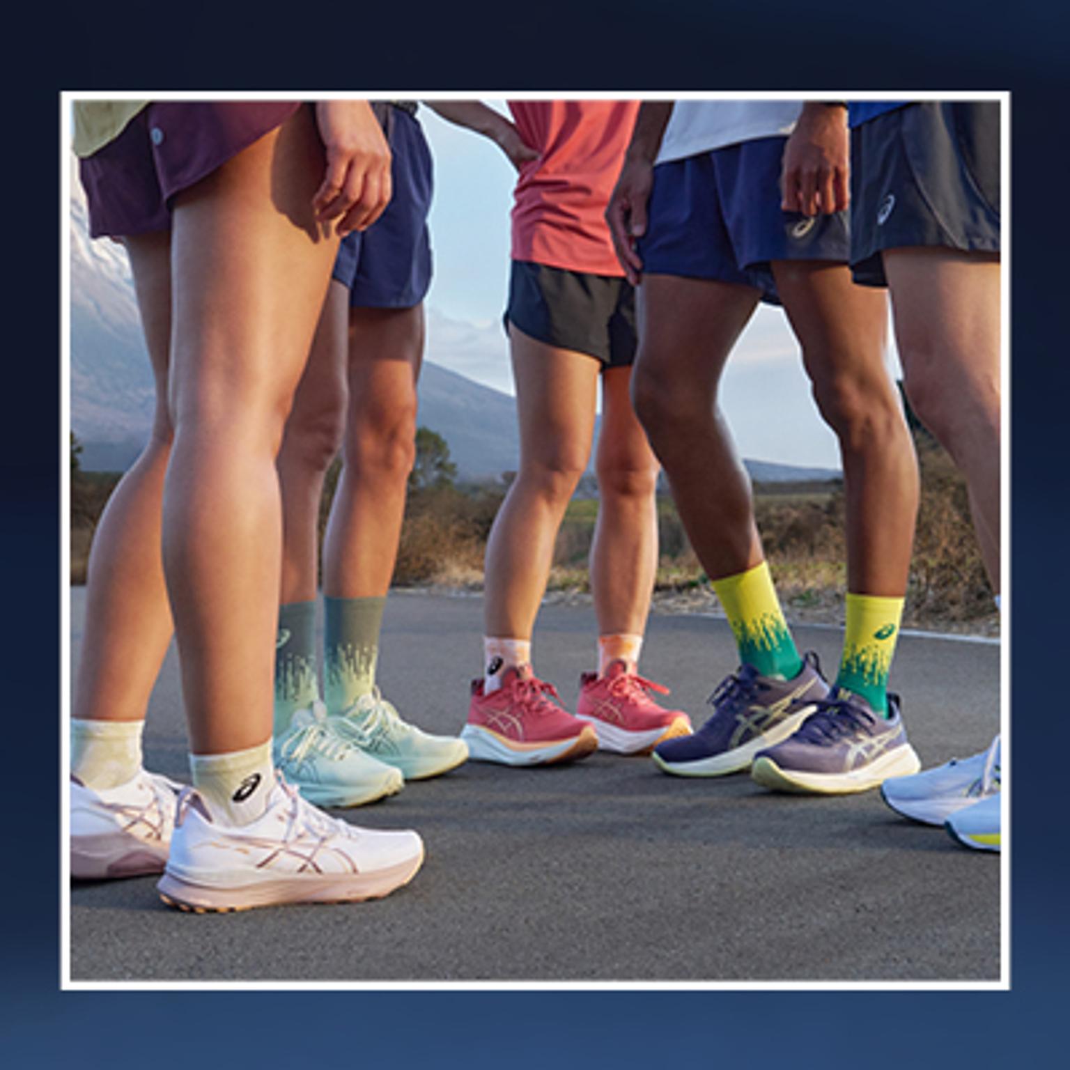 a group of people are standing next to each other on a road wearing asics shoes .