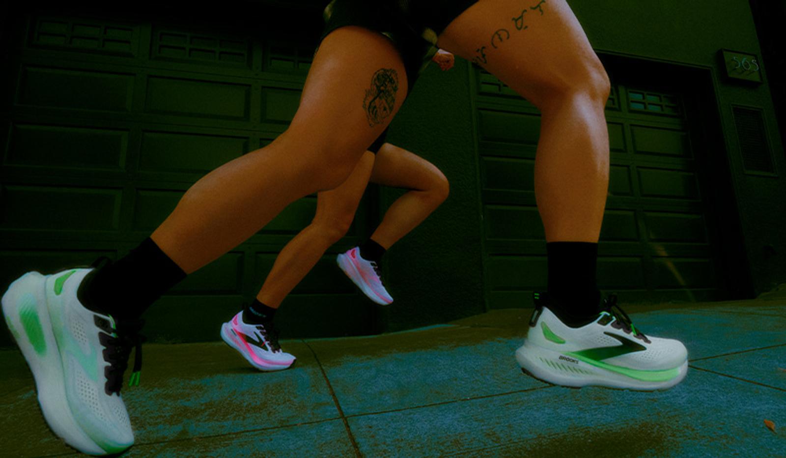 Low-angle view of two people running, showing their legs and running shoes; one pair is white and green, the other white and pink.