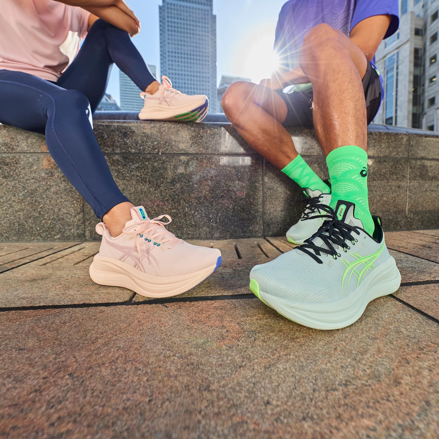 Two people sitting on a city ledge, wearing light pink and mint green running shoes.