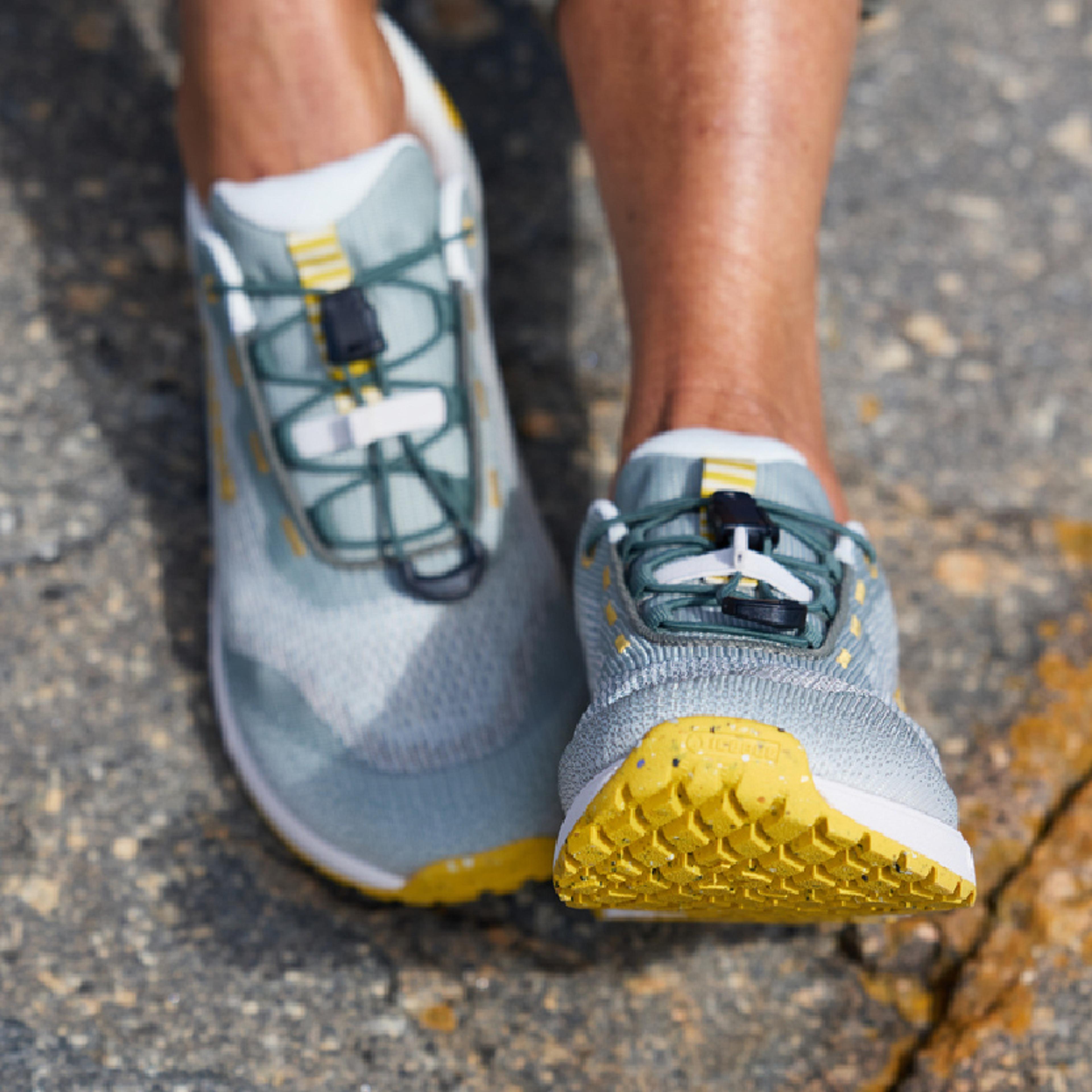 Light blue and yellow athletic shoes with bungee laces worn on feet.