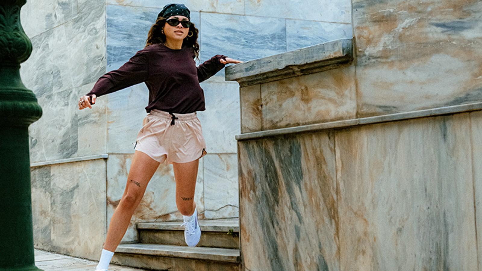 A woman in new shoes, a bandana, sunglasses, and activewear runs down marble steps.