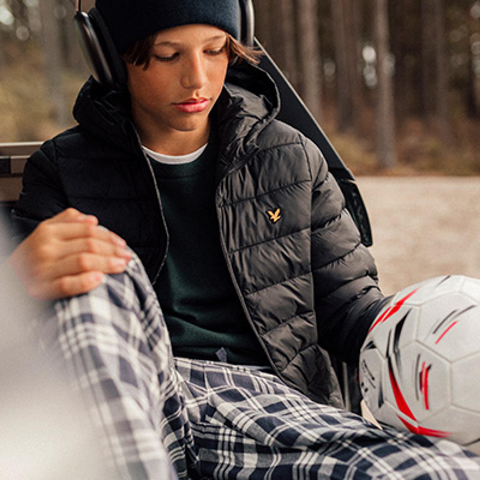 a young boy wearing headphones is sitting on a bench holding a soccer ball .
