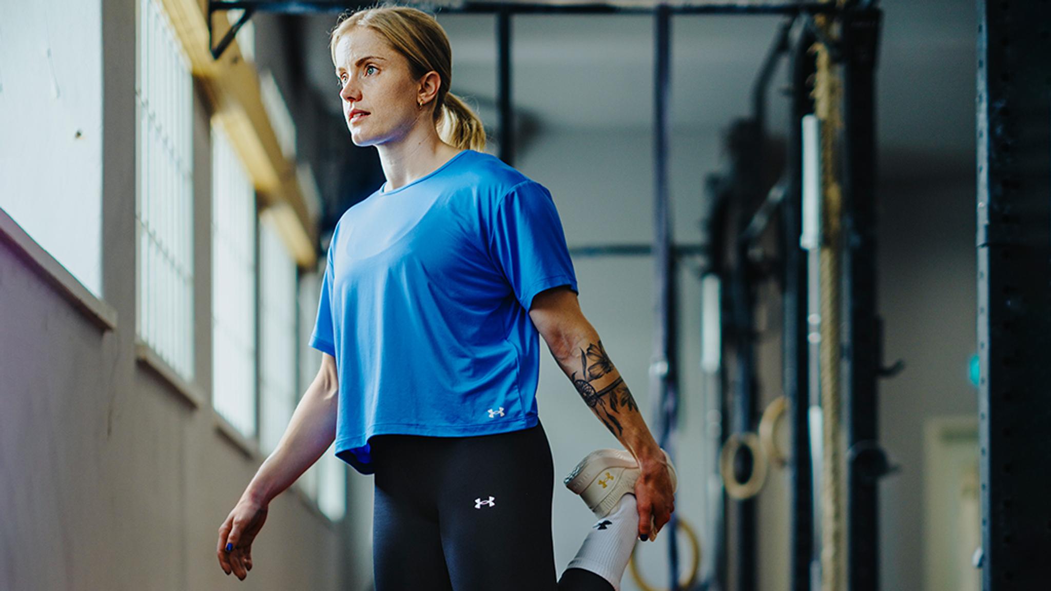 a woman in a blue shirt and black leggings is stretching her legs in a gym .