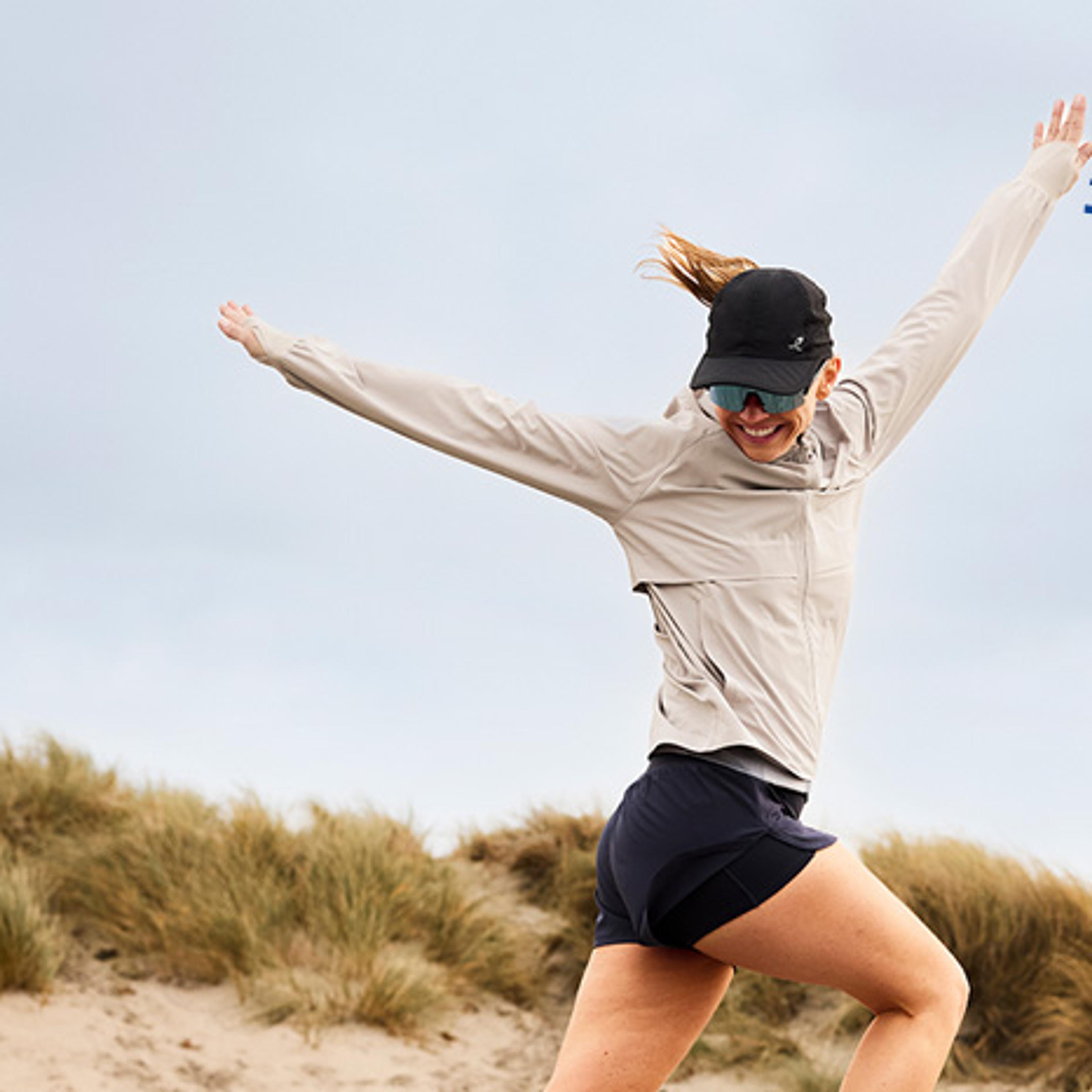 A smiling woman in athletic wear jumps on sandy dunes with the Intersport Experience logo.
