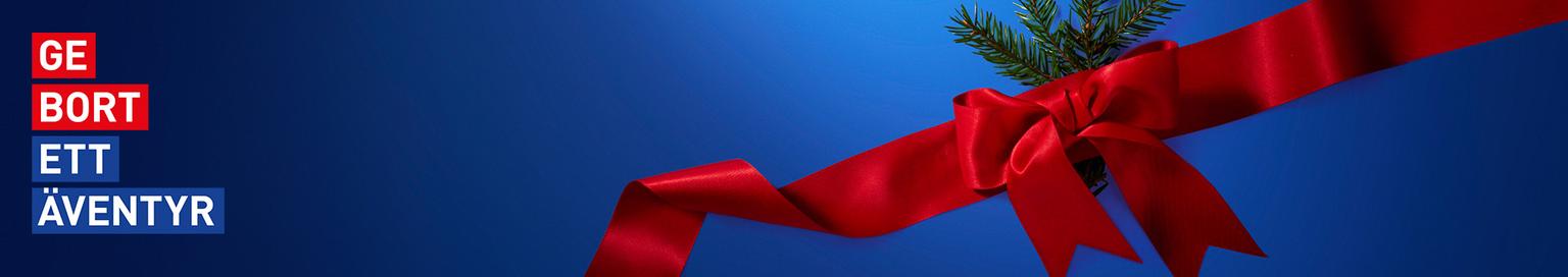 Blue banner with "GE BORT ETT ÄVENTYR" text on the left and a red gift ribbon with pine needles on the right.