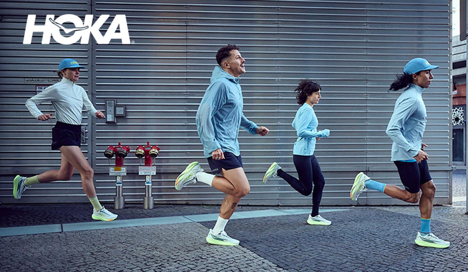 Four people wearing Hoka running shoes and athletic apparel jogging on a city street.