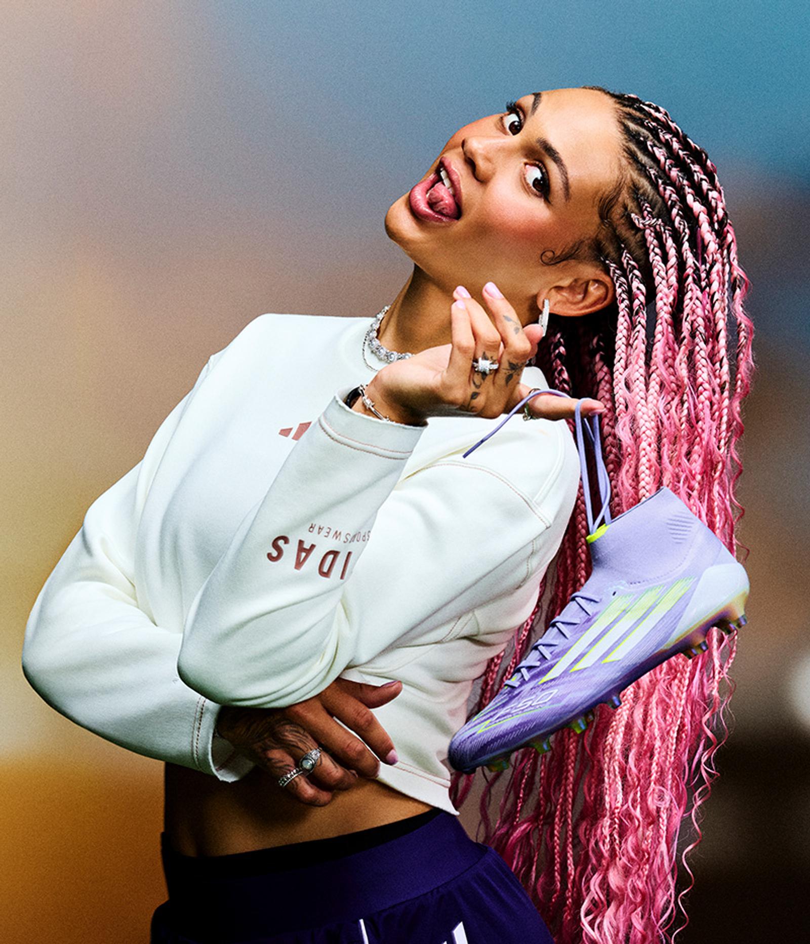 a woman with pink braids is holding a pair of adidas shoes
