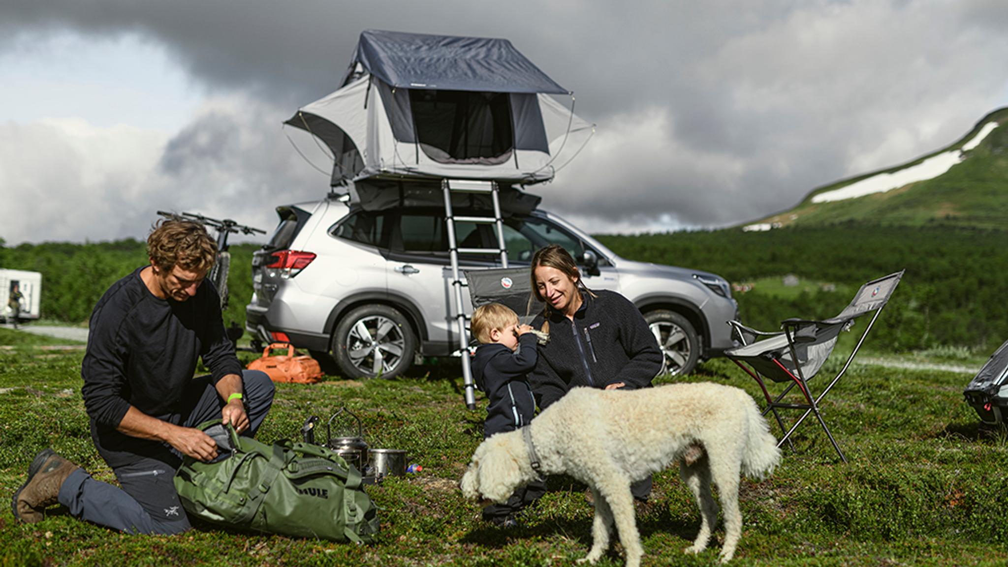 a family is camping with a tent on top of their suv .