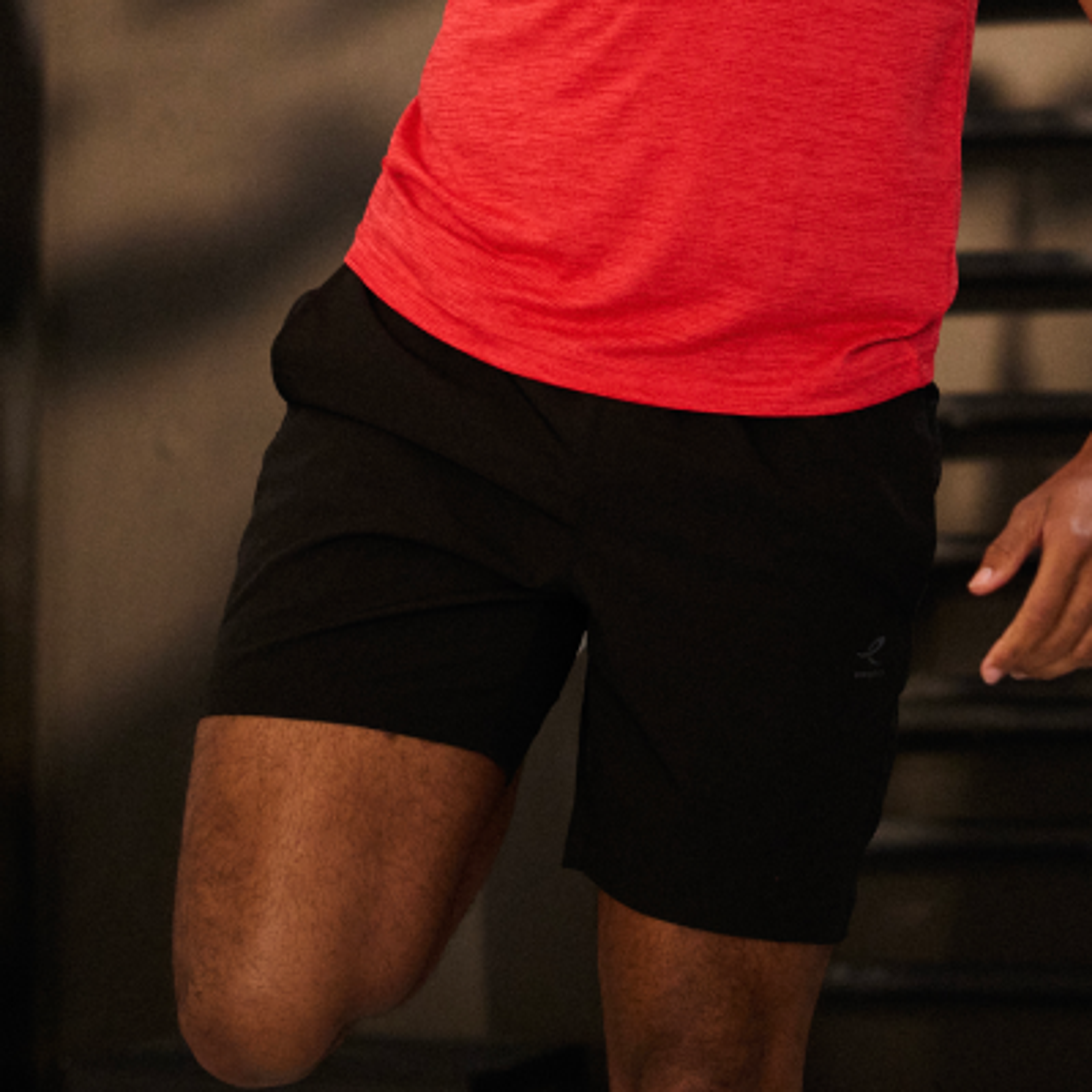 Person in a red shirt and black athletic shorts stretching one leg.