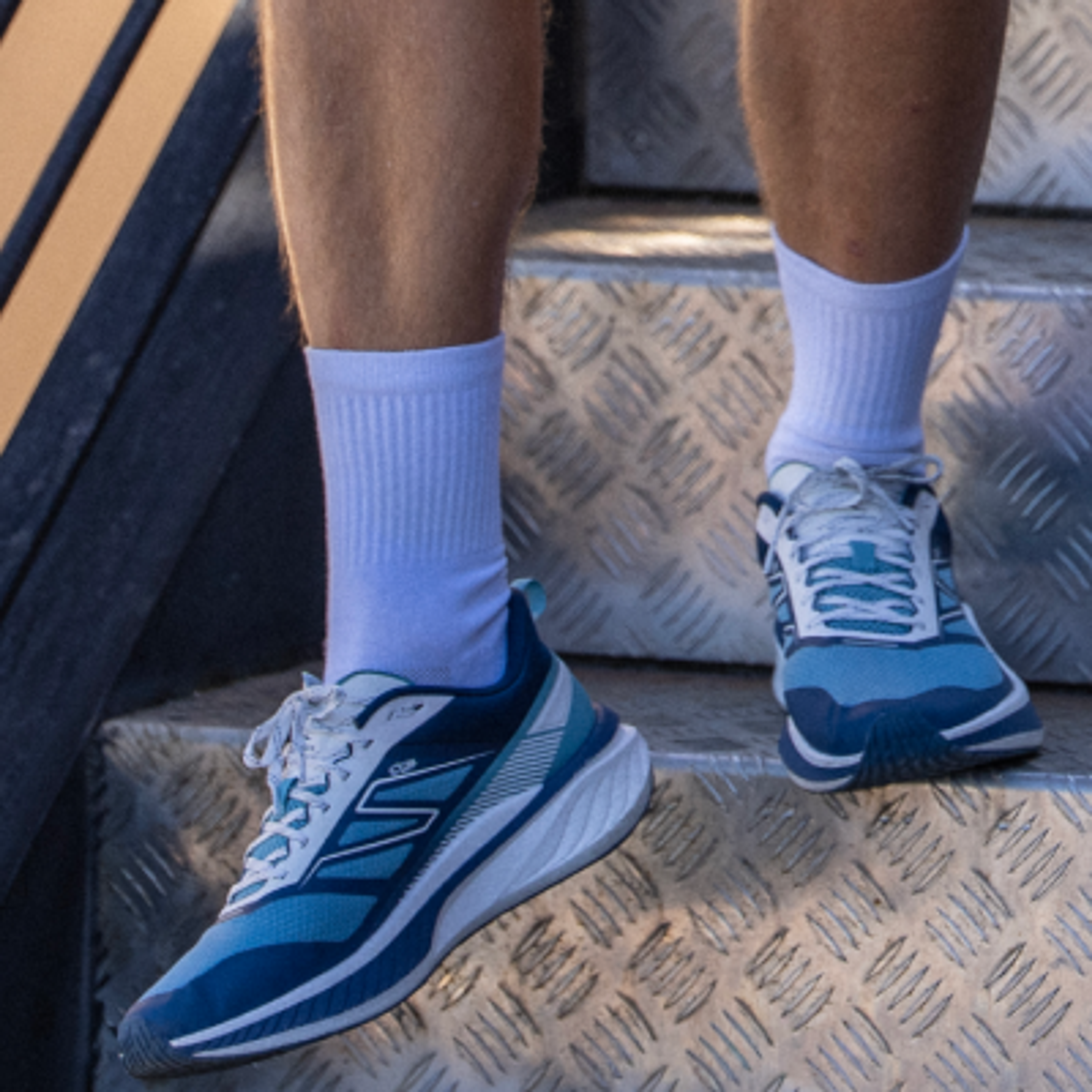 Legs wearing white socks and blue athletic shoes stepping down a metal staircase.
