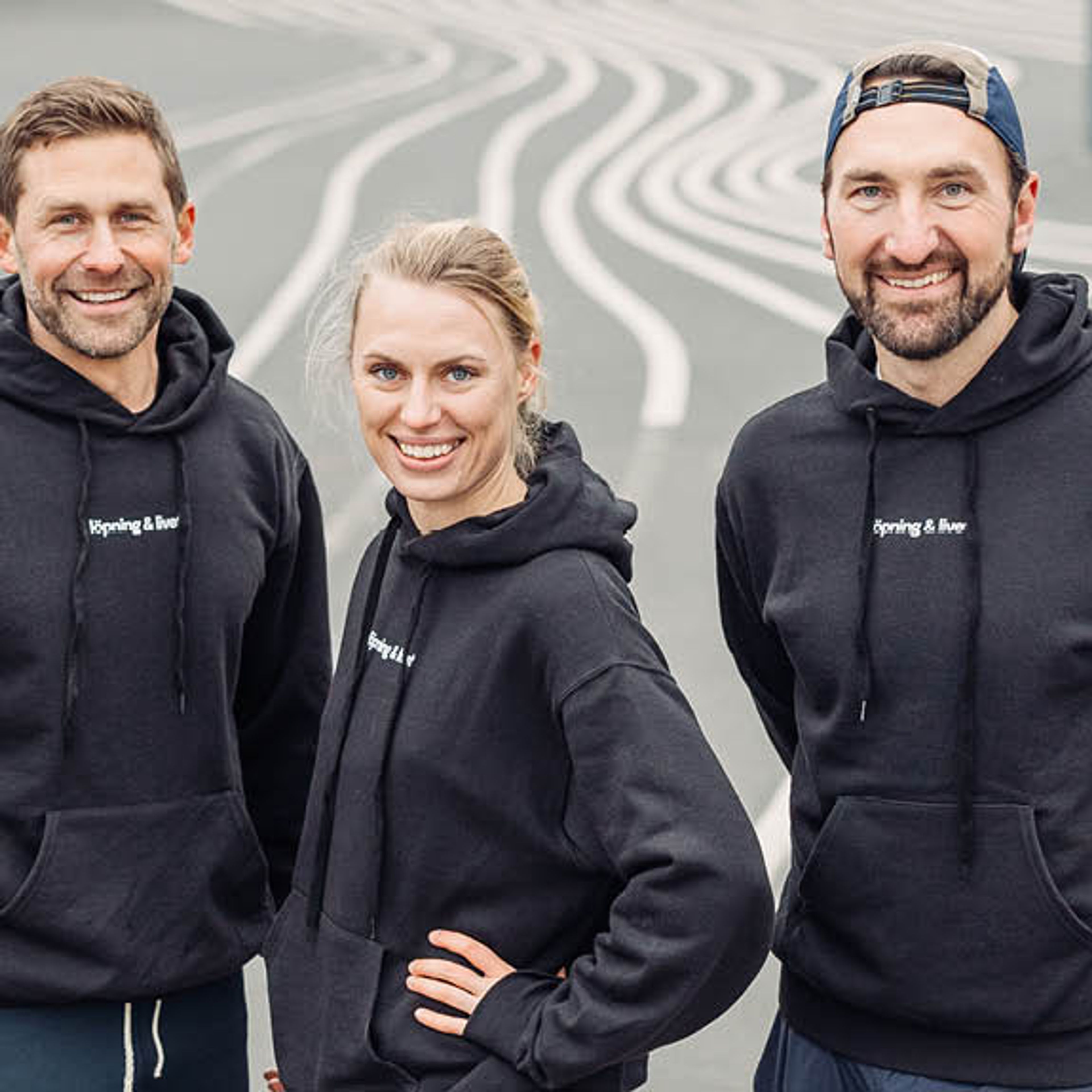 Three smiling people in black "running & beer" hoodies on a wavy-lined surface.