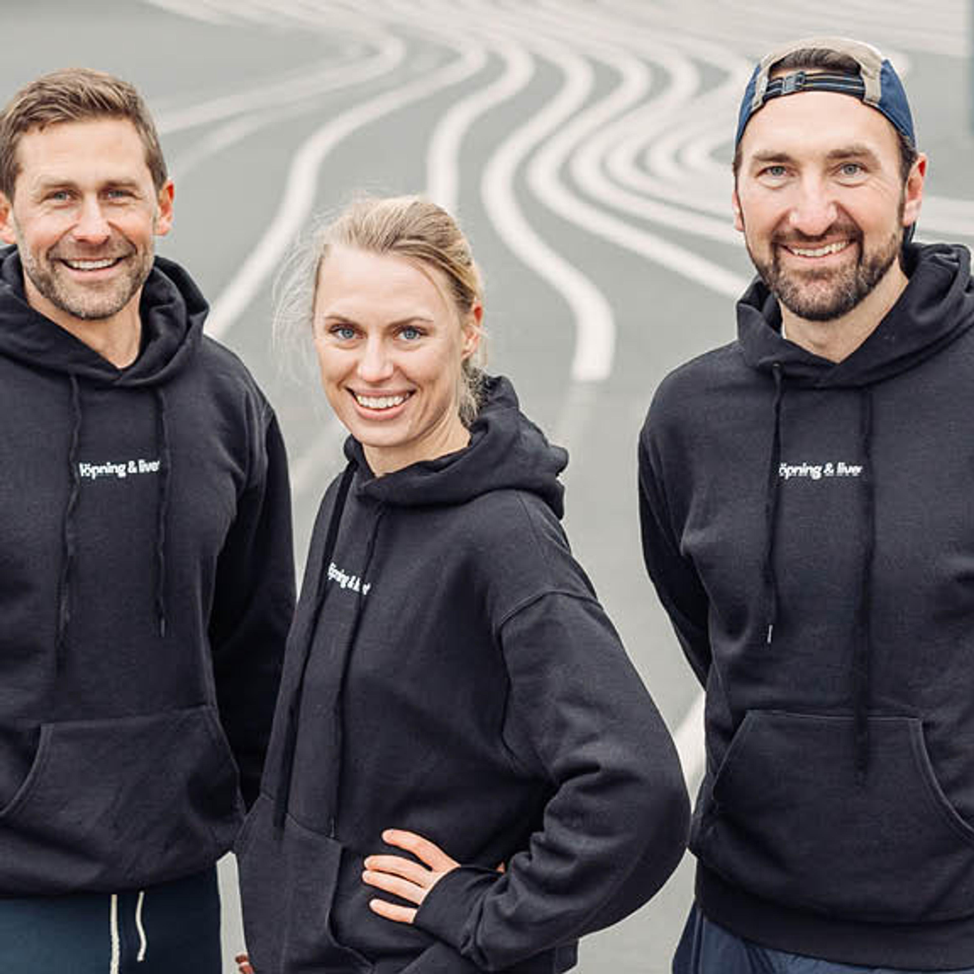 Three smiling people in black "running & beer" hoodies on a wavy-lined surface.