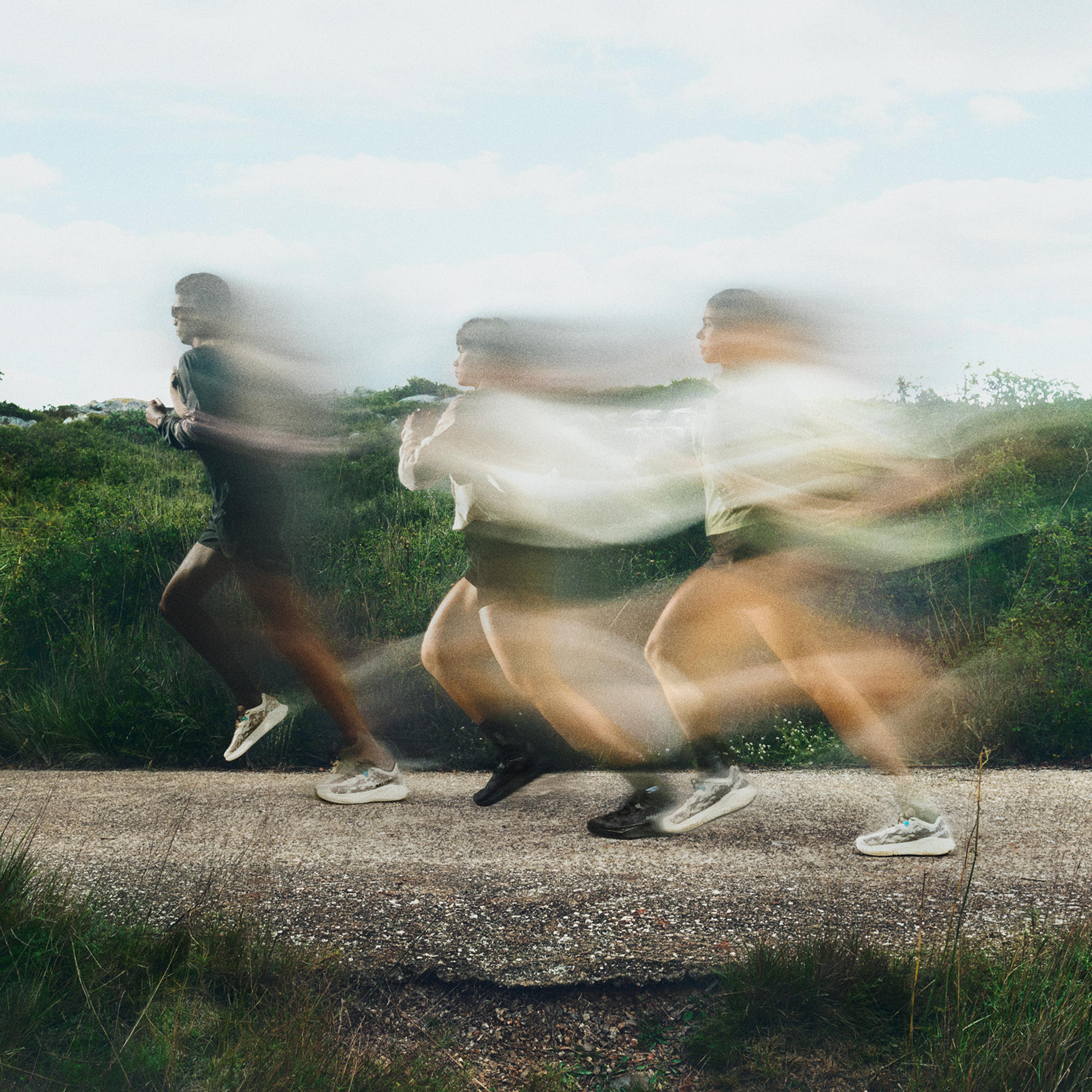Three blurred figures running quickly along an outdoor path with green foliage.
