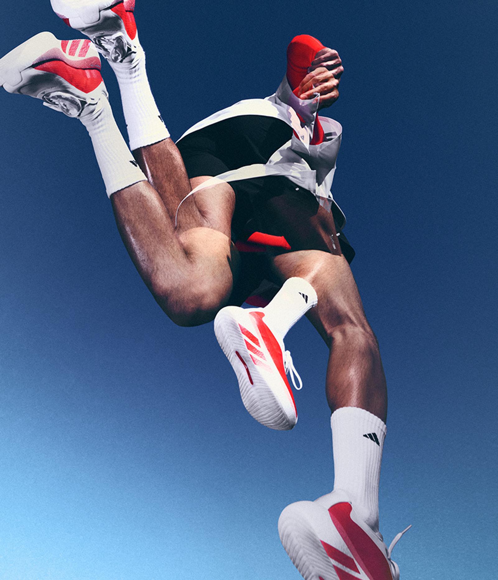 Person in white and red athletic shoes and gear mid-air, with multiple limbs suggesting dynamic motion, against a clear blue sky.